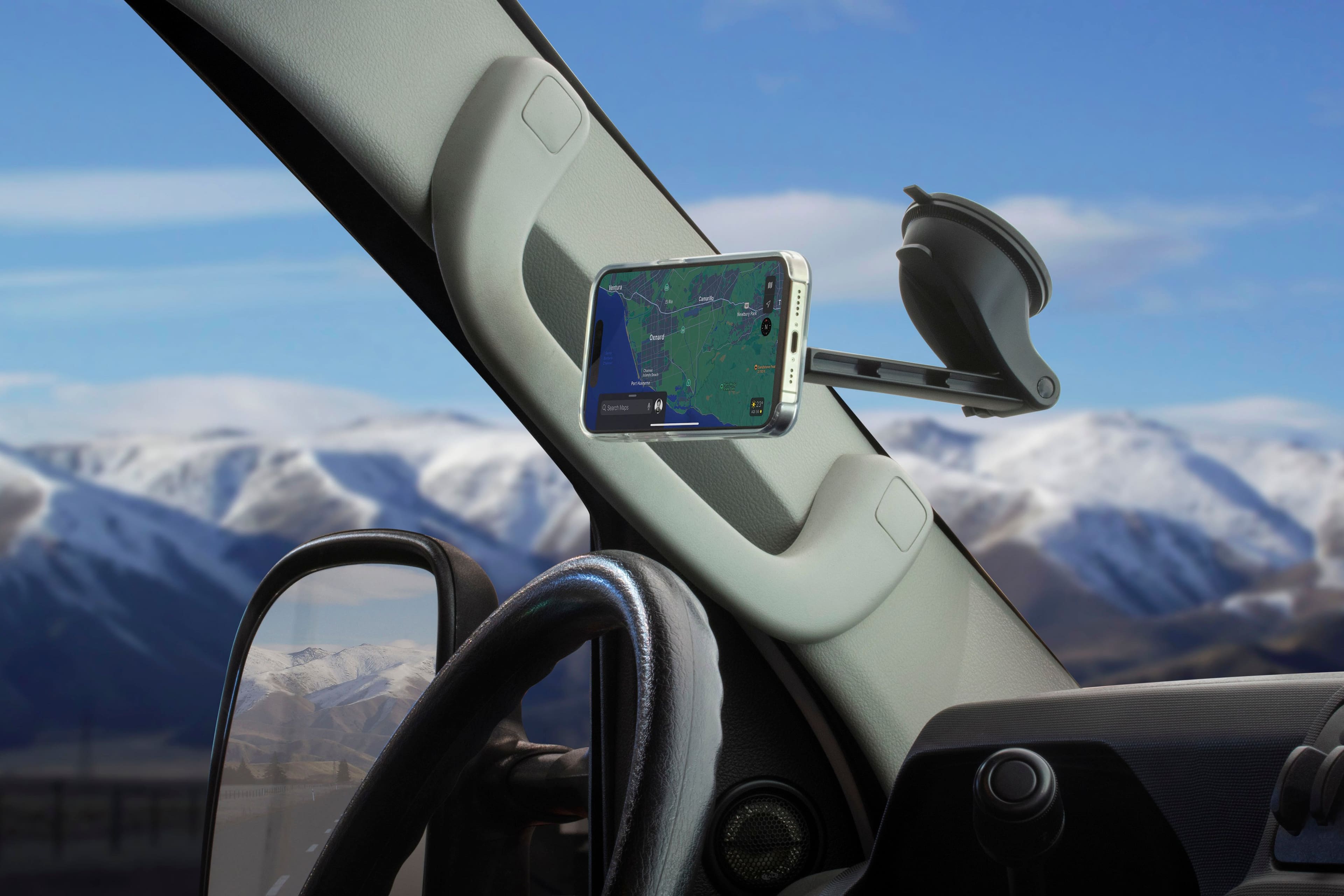 The image shows a car's dashboard with a cell phone mounted on a holder. The cell phone is displaying a map, possibly a GPS navigation system, and is positioned in the center of the dashboard. The car is likely driving down a mountain road, as the view of the mountains can be seen through the windshield. The car appears to be a convertible, with the top down, allowing the driver and passengers to enjoy the scenic view.