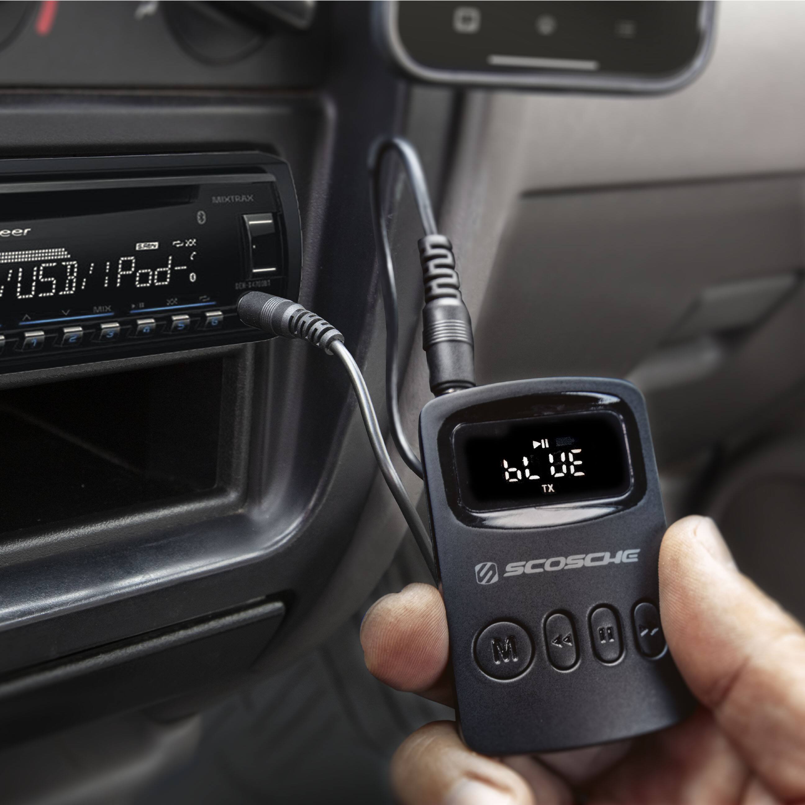 The image features a person holding a black device with a USB connection, which is likely an iPod or a similar device. The device is connected to a car's stereo system, as indicated by the presence of a car radio in the background. The person is likely using the device to control their music or other media while driving or traveling.