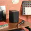 The image features a black speaker on a wooden table, accompanied by a microphone. There is also a book and a record nearby. The text on the image reads "PEB APRIL 22 TRY $13 E INFO AT ROCKCLUR COM r00 Midnight Ladies 3O? e AZAA READER POGALYPS JAMES PATTERSON universar EDIFIER."