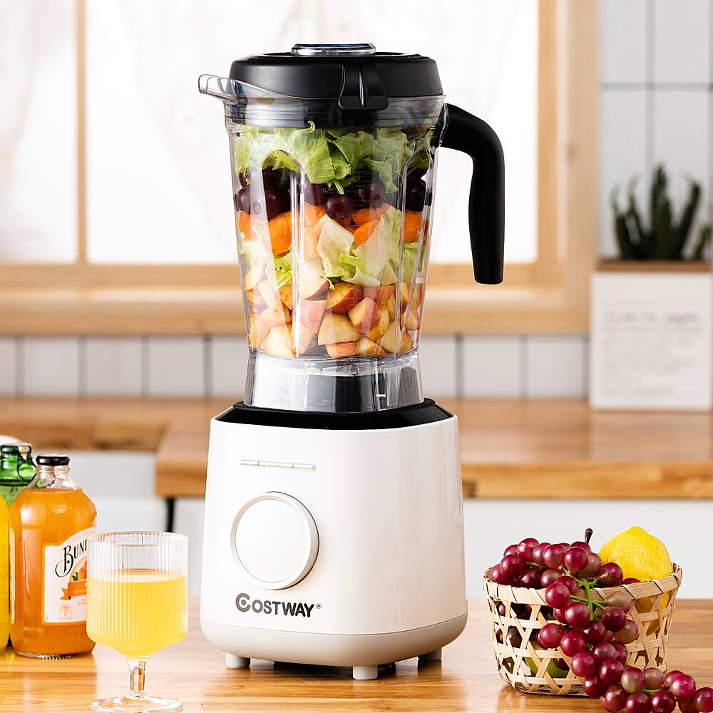 A blender full of vegetables and fruits sits on a counter next to a bottle of juice and a glass of juice.