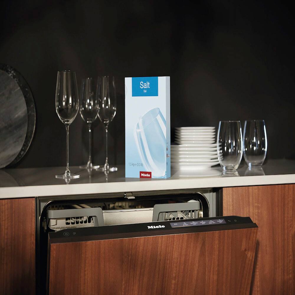 The image features a dishwasher with a box of salt placed on top of it. The salt is specifically designed for use with Miele dishwashers, ensuring optimal performance and cleaning results. The dishwasher is surrounded by various wine glasses, which are likely to be used for entertaining or enjoying a meal. The presence of the salt box and the wine glasses suggests that the dishwasher is well-maintained and ready for use.