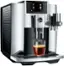 The image shows a Jura E8 coffee machine with a glass of coffee sitting on top of it. The machine is silver and black in color, and it is equipped with a digital display. The coffee is being brewed, and the machine is ready to serve a hot beverage.