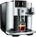 The image shows a Jura E8 coffee machine with a glass of coffee sitting on top of it. The machine is silver and black in color, and it is equipped with a digital display. The coffee is being brewed, and the machine is ready to serve a hot beverage.