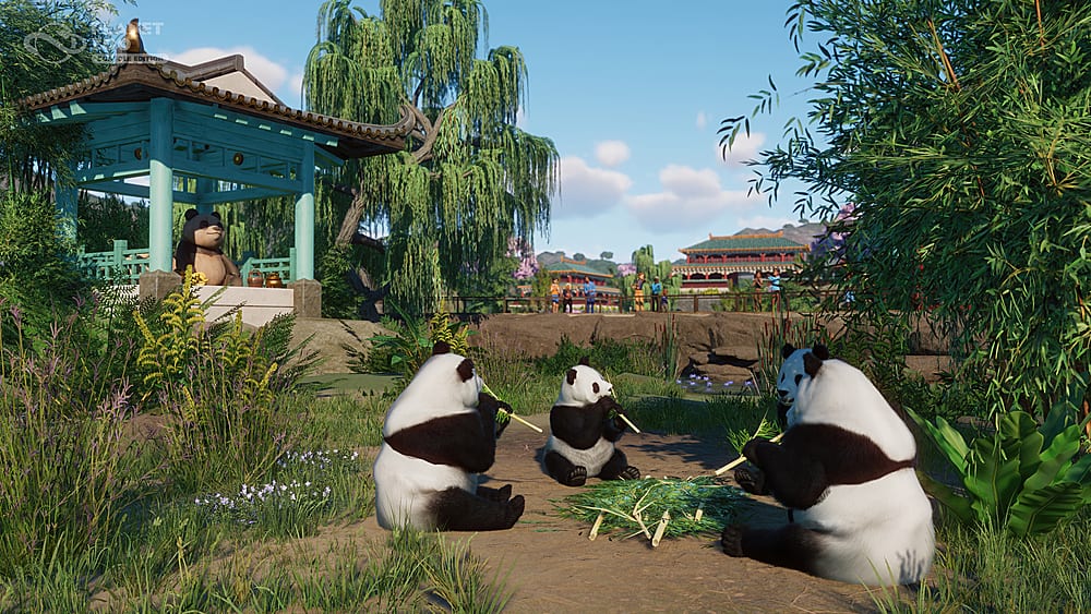 The image shows three panda bears sitting in a grassy area, with a pavilion in the background. The bears are surrounded by trees and bushes, creating a natural habitat for them. The scene appears to be a peaceful and serene environment, with the pandas enjoying their time together.