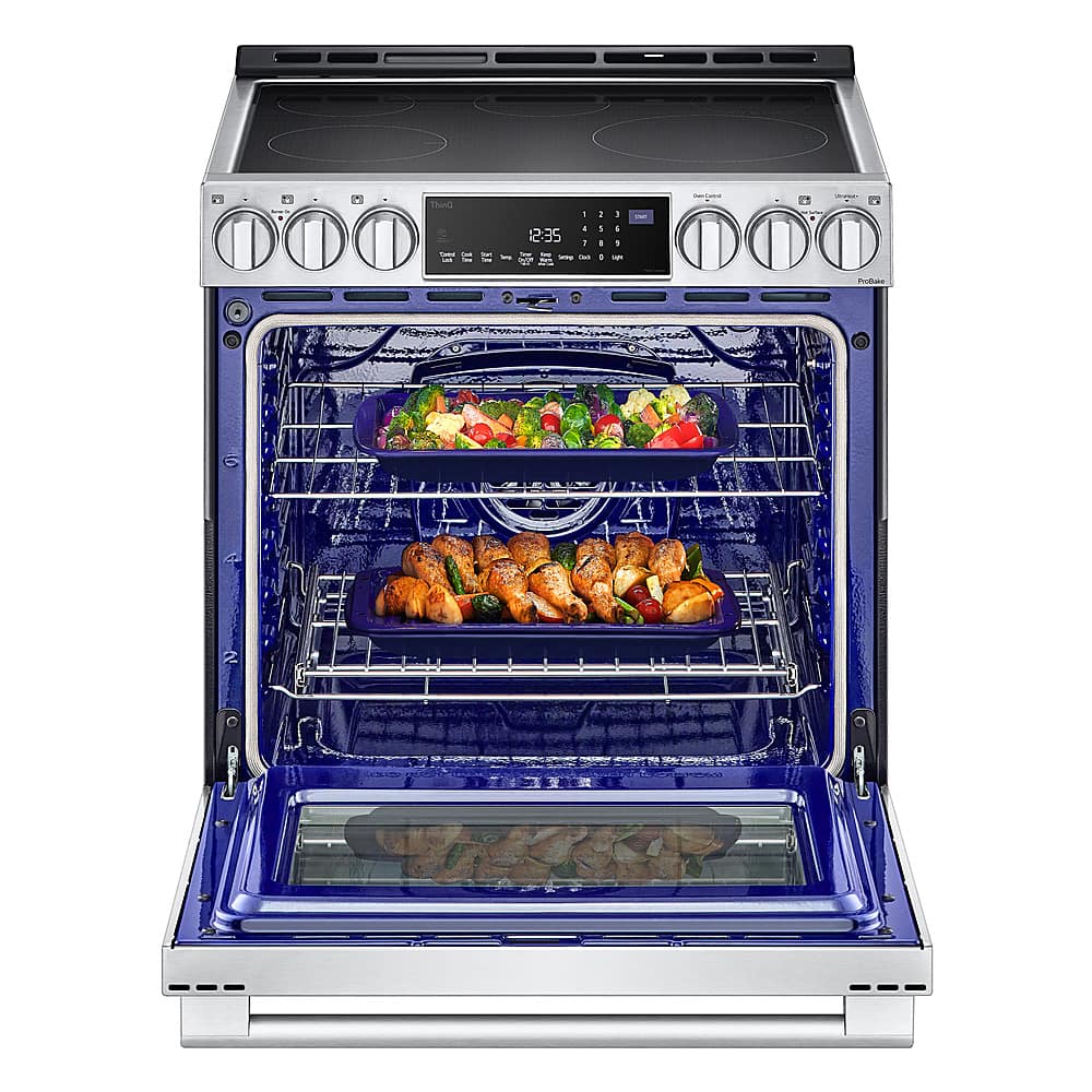 The image shows a blue oven with two trays of food inside. The oven is open, revealing the delicious meal being cooked. The food includes chicken and vegetables, making it a colorful and appetizing sight. The oven is placed in a kitchen setting, and the food is being cooked at 12:35.
