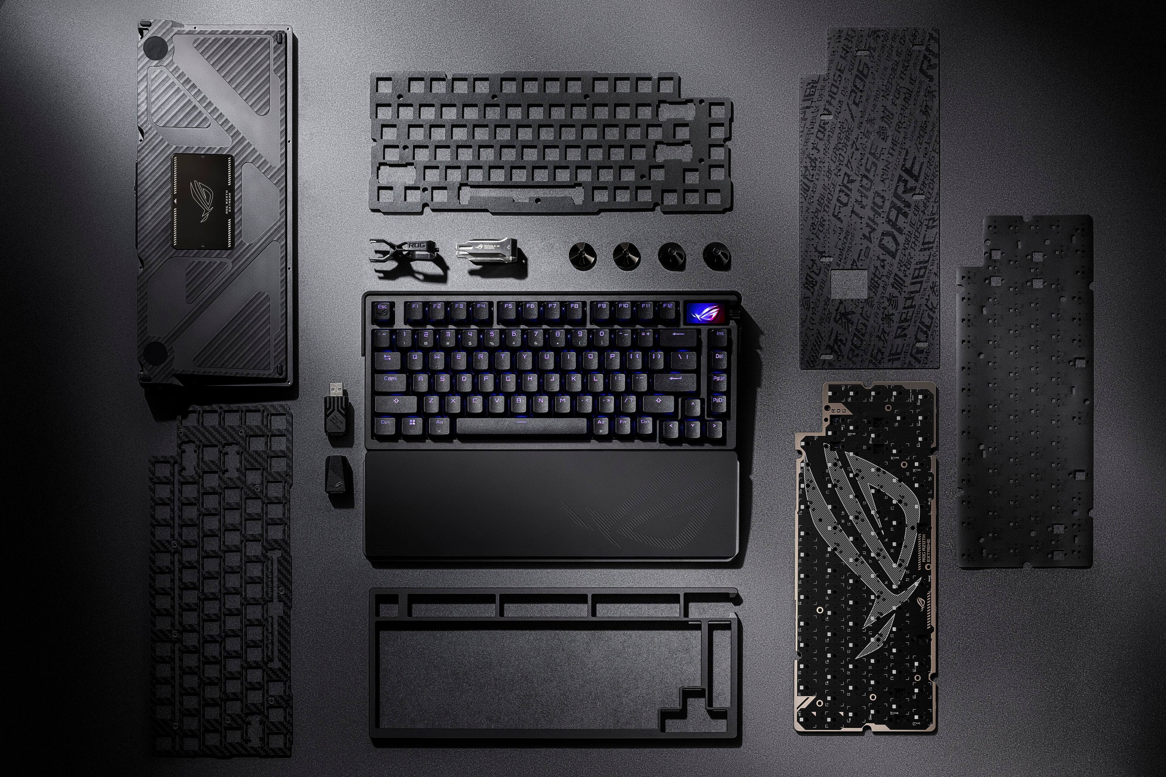 The image shows a computer keyboard and its components laid out on a table. The keyboard is disassembled, revealing its internal parts. The components include a spacebar, a shift key, an enter key, and a number pad. The keyboard is accompanied by a laptop, which is also disassembled, showcasing its internal components. The scene appears to be a close-up view of the computer keyboard and laptop, highlighting their intricate details and structure.