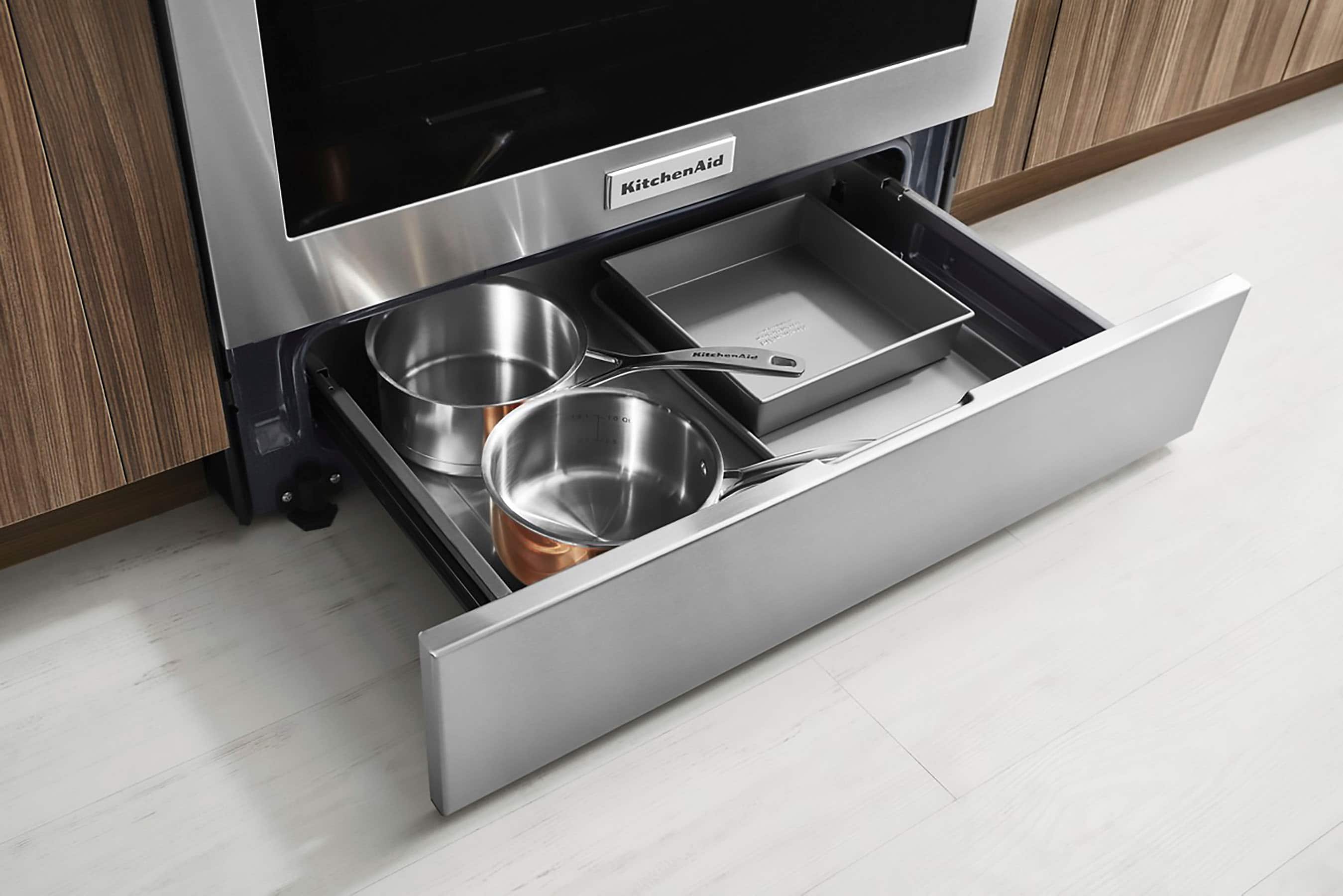 The image features a kitchen with a built-in stainless steel oven and microwave. The oven has a silver handle and a drawer with a silver pot and pan set. The microwave is located above the oven, and the kitchen appears to be well-organized and functional.