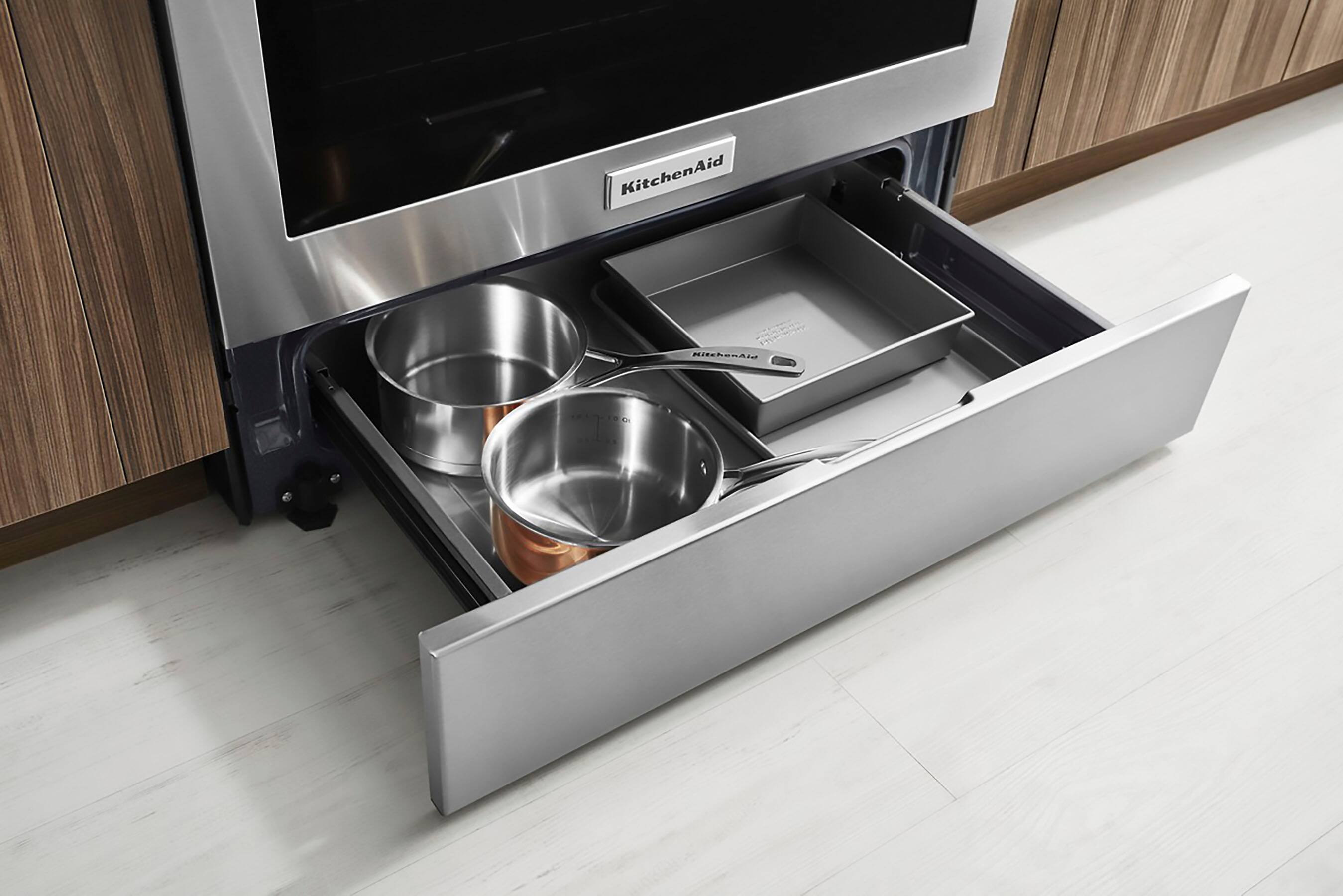 The image features a kitchen with a built-in stainless steel oven and microwave. The oven has a silver handle and a drawer with a silver pot and pan set. The microwave is located above the oven, and the kitchen appears to be well-organized and functional.