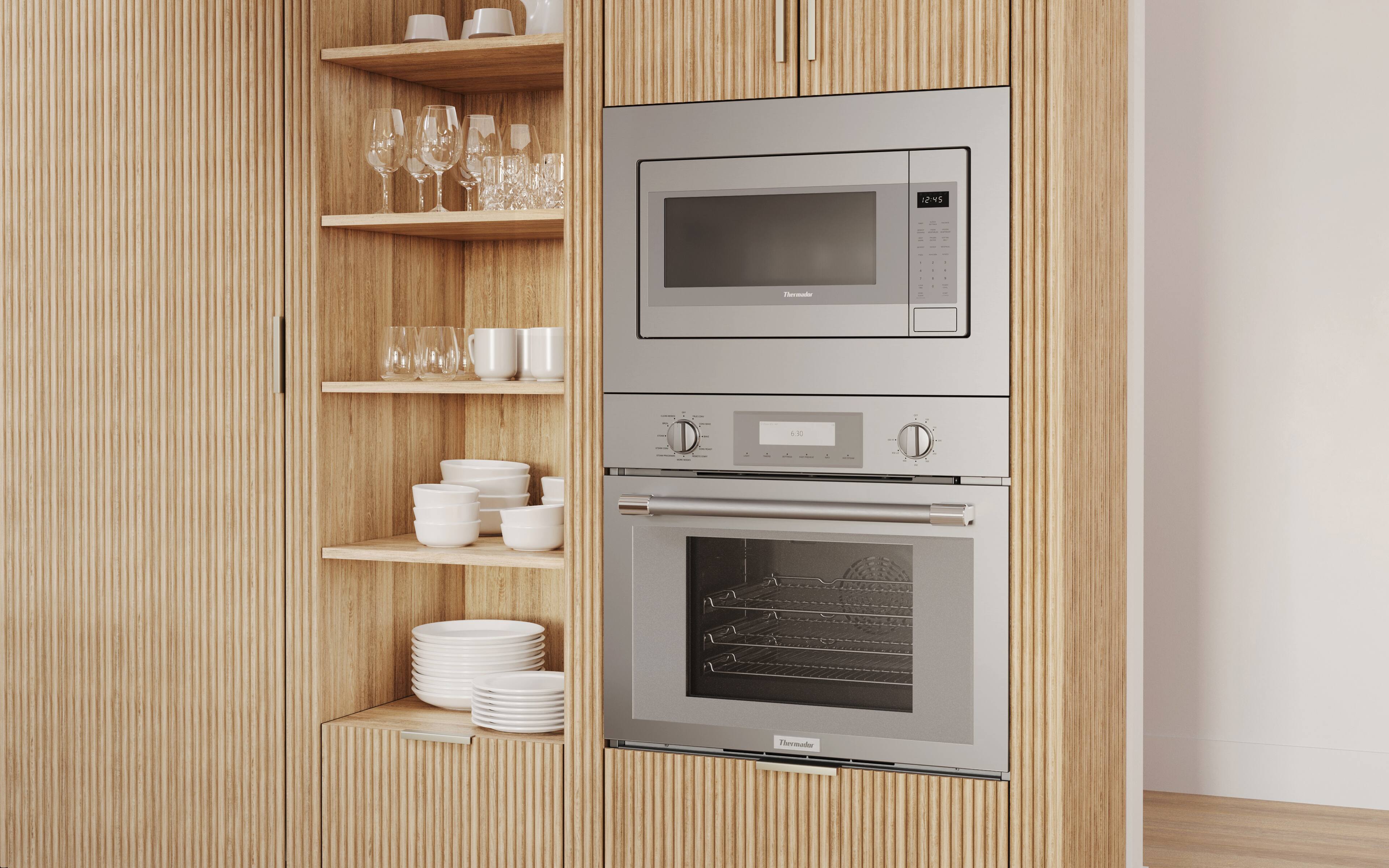 The image features a kitchen with a stainless steel oven and a microwave above it. The oven is positioned under a wooden cabinet with a shelf, where several wine glasses are neatly arranged. The microwave is placed above the oven, and the kitchen appears to be well-organized and clean.