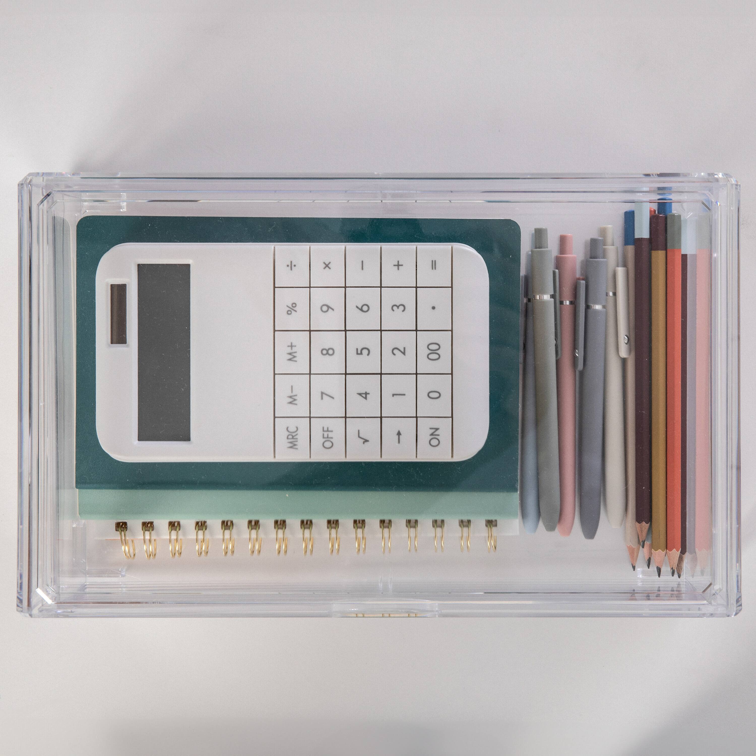 The image shows a calculator and a notebook with pens and pencils. The calculator has a green and white color scheme. The notebook is green and white as well, and it contains pens and pencils. The calculator has a clear case, and the notebook is placed on a table.