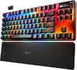 The image features a black keyboard with a rainbow-colored design. The keyboard has a unique design, with the keys featuring a combination of white, red, blue, yellow, and green colors. The keyboard is placed on a black stand, which adds to the overall aesthetic of the setup. The keyboard is made by Steelseries, a well-known brand in the gaming industry.