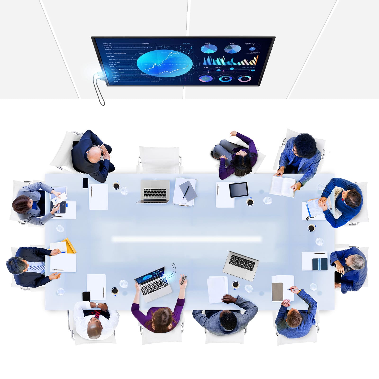 The image shows a group of people sitting around a large table, each with a laptop in front of them. There are several cups and books on the table, indicating that they might be working or discussing something. The people are wearing ties, suggesting a formal or professional setting. The table is surrounded by chairs, and there is a TV mounted on the wall above the table. The scene appears to be a conference room or a meeting area where people gather to collaborate or discuss various topics.