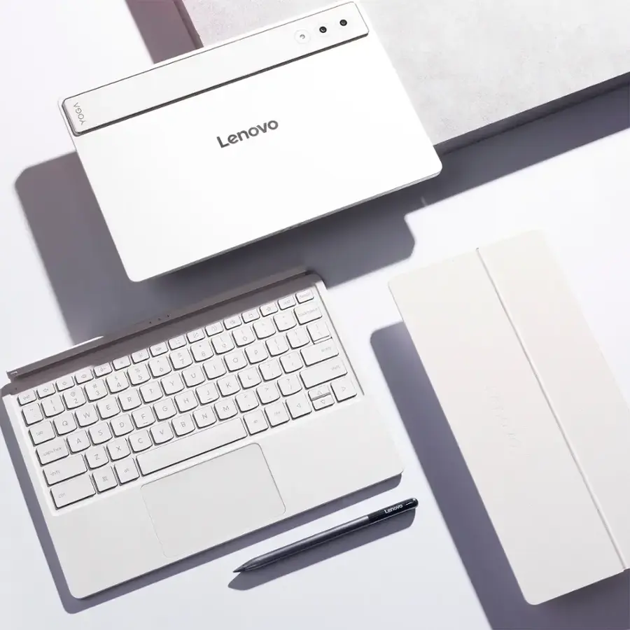 Lenovo is the brand of the laptop and the keyboard in the image. The laptop is white, and it is sitting next to a white keyboard. The laptop and keyboard are placed on a white surface, possibly a table.