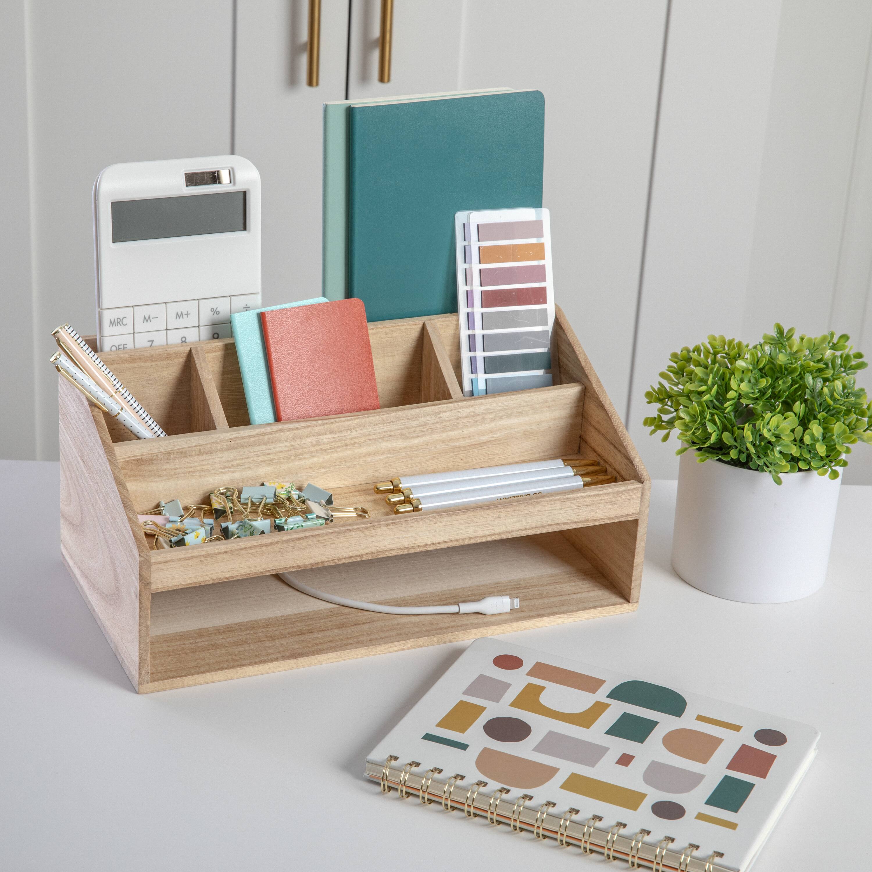 The image shows a wooden desk organizer with various items in it, including a notebook, a book, a calculator, and a pencil. The organizer is placed on a white table, and there is a potted plant nearby. The desk organizer is filled with different items, making it a functional and well-organized workspace.