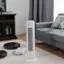 The image shows a living room with a small white fan on the floor, next to a couch. There is a laptop placed on the couch, and a book is also present in the scene. The room appears to be well-organized and comfortable, with the fan providing a source of cooling or ventilation.