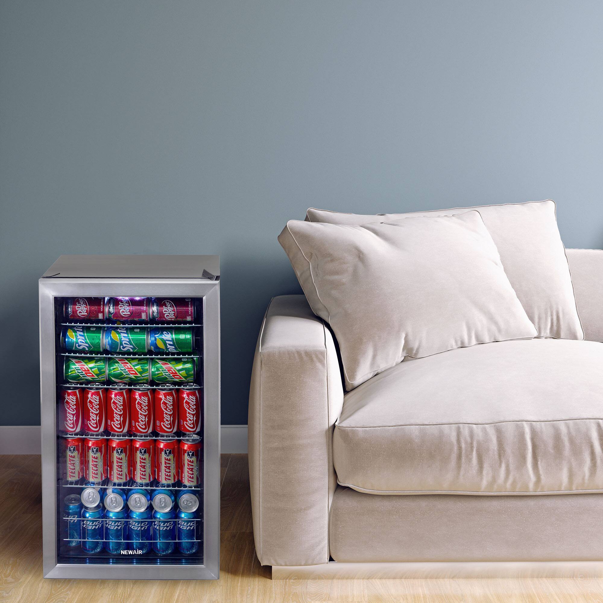 The image shows a couch with a small refrigerator or cooler next to it. The cooler is filled with various drinks, including Coca-Cola, Sprite, and Fanta. There are a total of 12 drinks in the cooler, with 6 Coca-Cola, 3 Sprite, and 3 Fanta. The couch is positioned in front of a wall, and the scene appears to be in a living room.