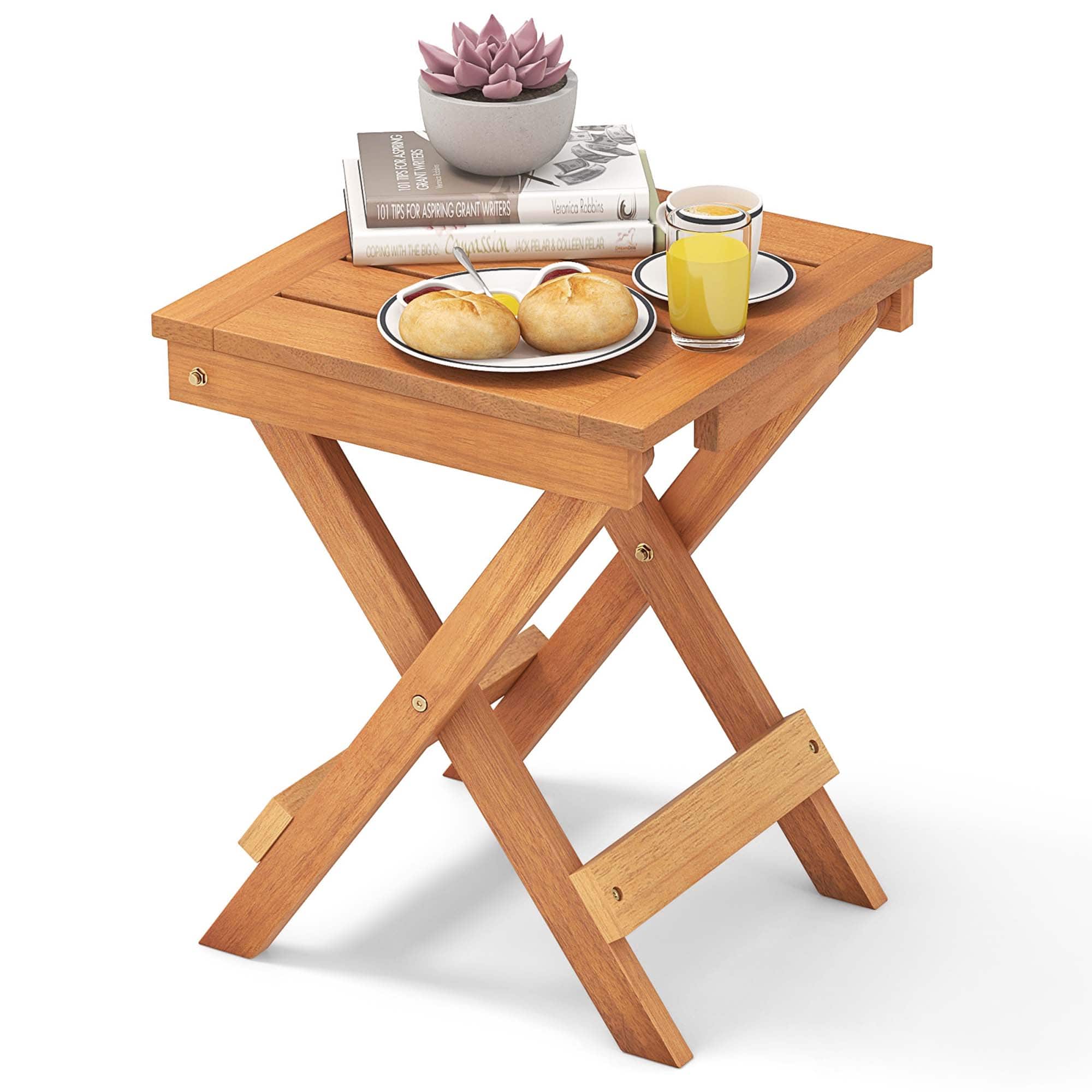 The image features a wooden tray table with a bowl of food and a plate of bread. The table is placed on a wooden floor, and there is a book nearby. The food on the table includes a sandwich and a cup of juice. Additionally, there is a potted plant in the background, adding a touch of greenery to the scene. The overall setting suggests a cozy and inviting atmosphere for enjoying a meal or a snack.