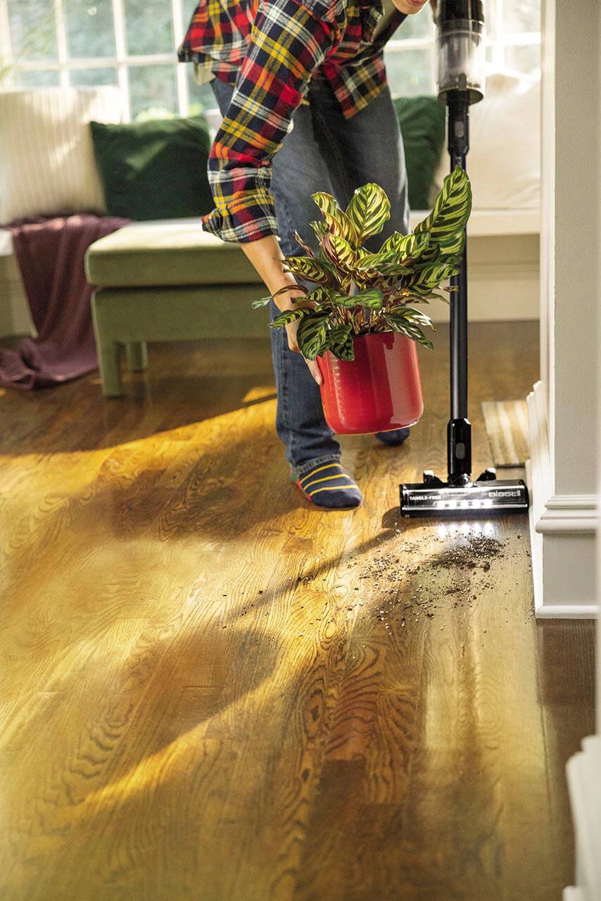 The text on the image reads "Tanole-F missel." However, it is not clear what this text represents or its relevance to the image. The image shows a person using a vacuum cleaner to clean the floor, with a potted plant nearby.