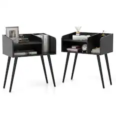 The image shows two small black tables with shelves in them. The tables are placed on top of black legs and have various items on them. There are two books on each table, with one book placed on the left side and the other on the right side. Additionally, there are two clocks, one on the left table and the other on the right table. A cup is also present on the left table. The tables are arranged in a way that they can be used as a desk or a side table.