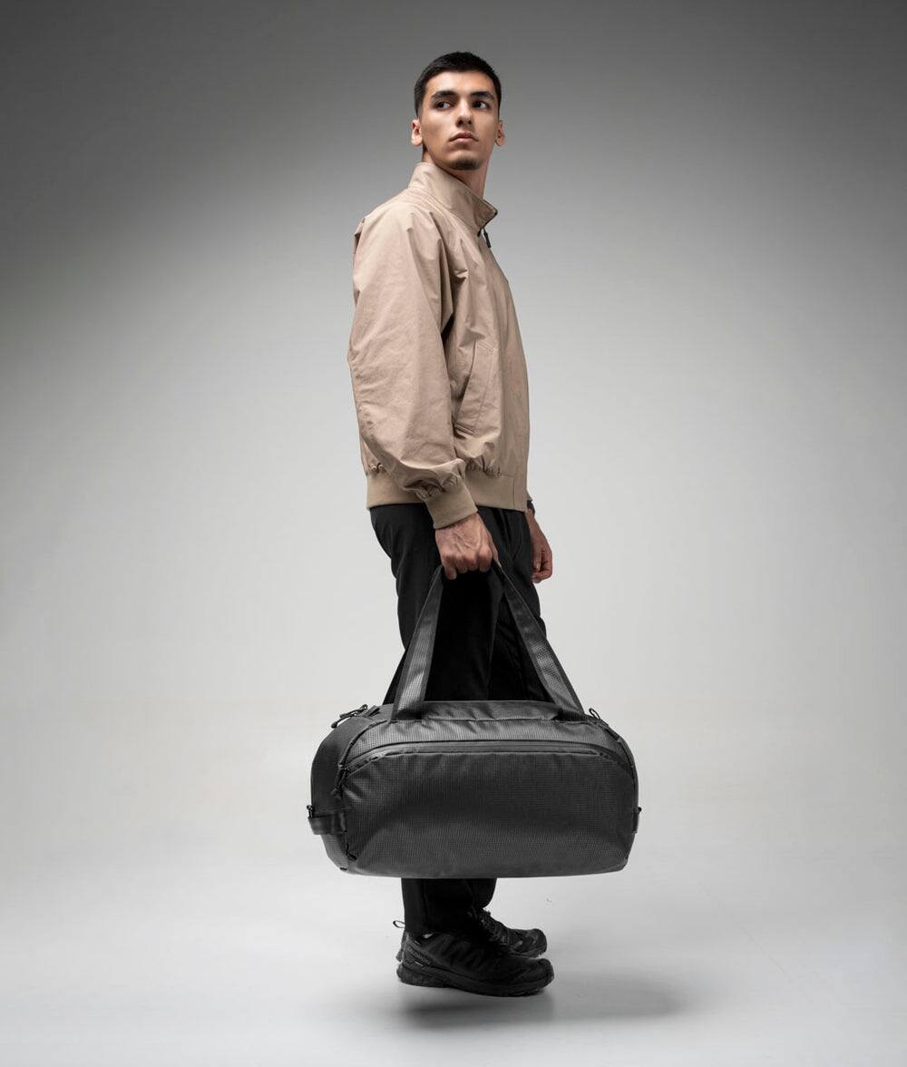 Angle. ALPAKA - 35L Lightweight Duffel Bag for Gym, Weekend Trips & Carry-On Travel, Momentum Duffel, Weather-Resistant - Axodyne hybrid Black.