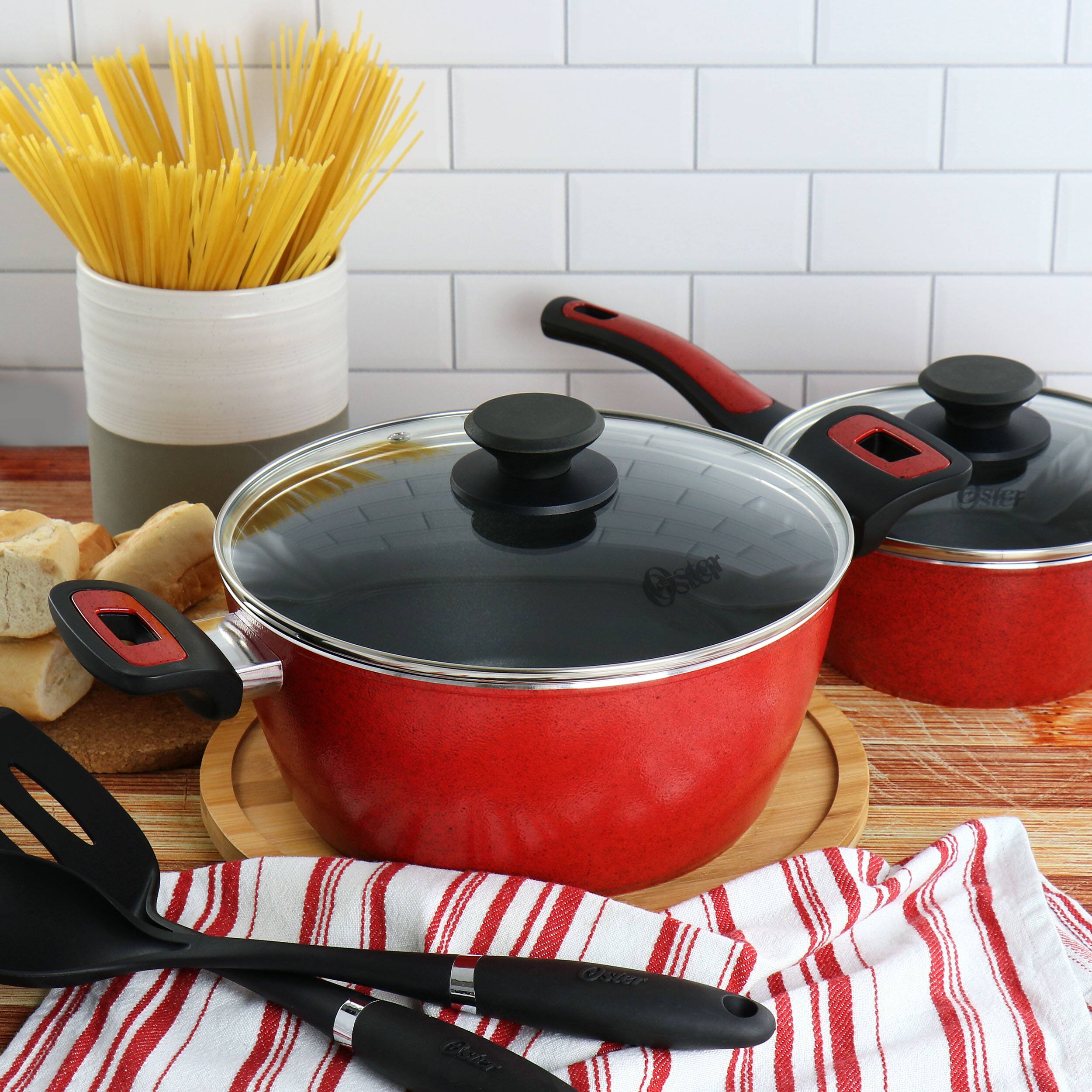 The image features a red pot on a wooden table, accompanied by a spoon and a fork. The pot is placed on a cutting board, and there is a bowl nearby. Additionally, there are two other pots on the table, one of which is a red pot. The table also has a basket of pasta and a loaf of bread.