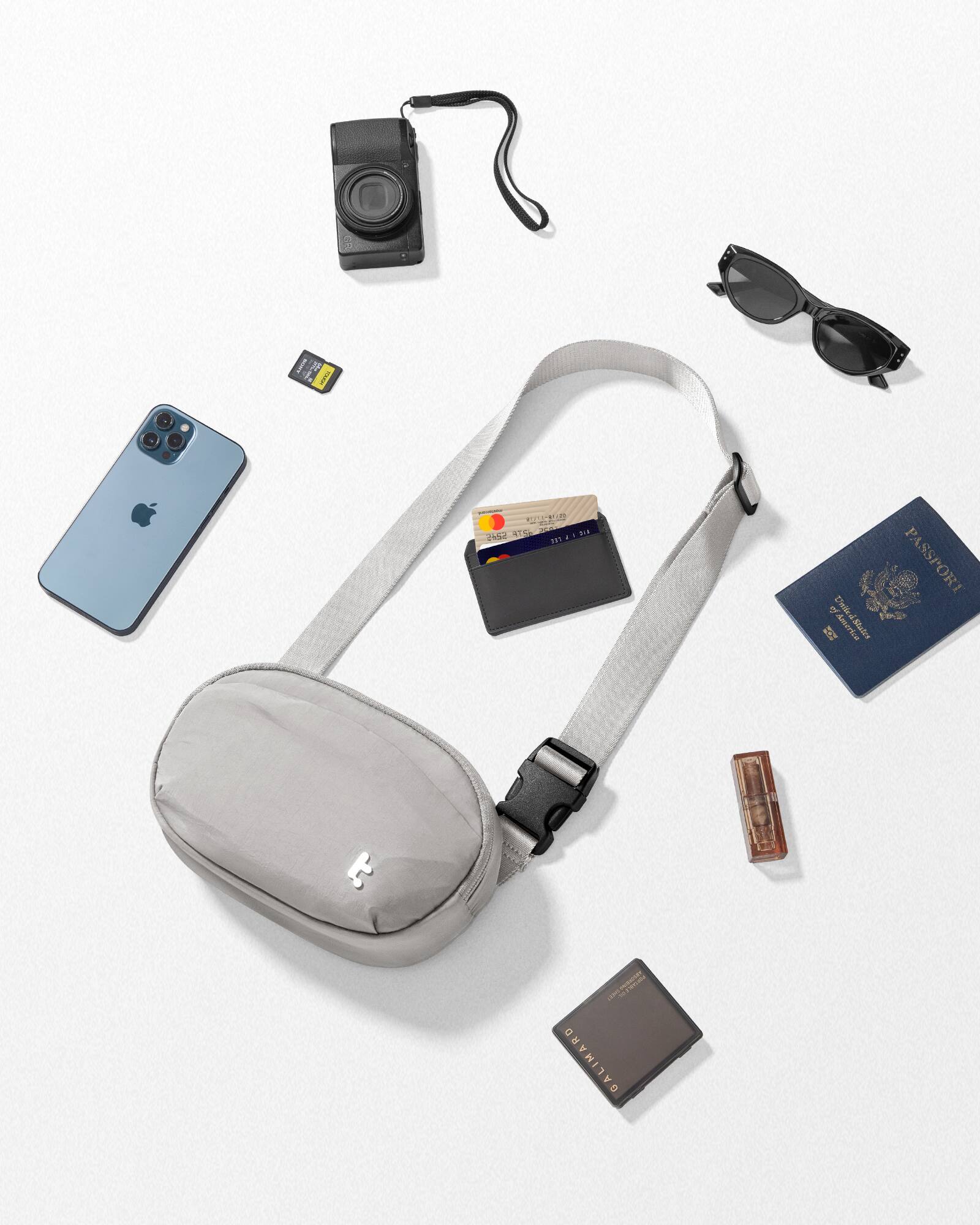 The image features a variety of items, including a passport, a wallet, a cell phone, a camera, sunglasses, and a bag. The passport is located on the right side of the image, while the wallet is positioned towards the center. The cell phone is situated on the left side, and the camera is placed in the middle. The sunglasses are located towards the top right corner, and the bag is placed in the bottom left corner.