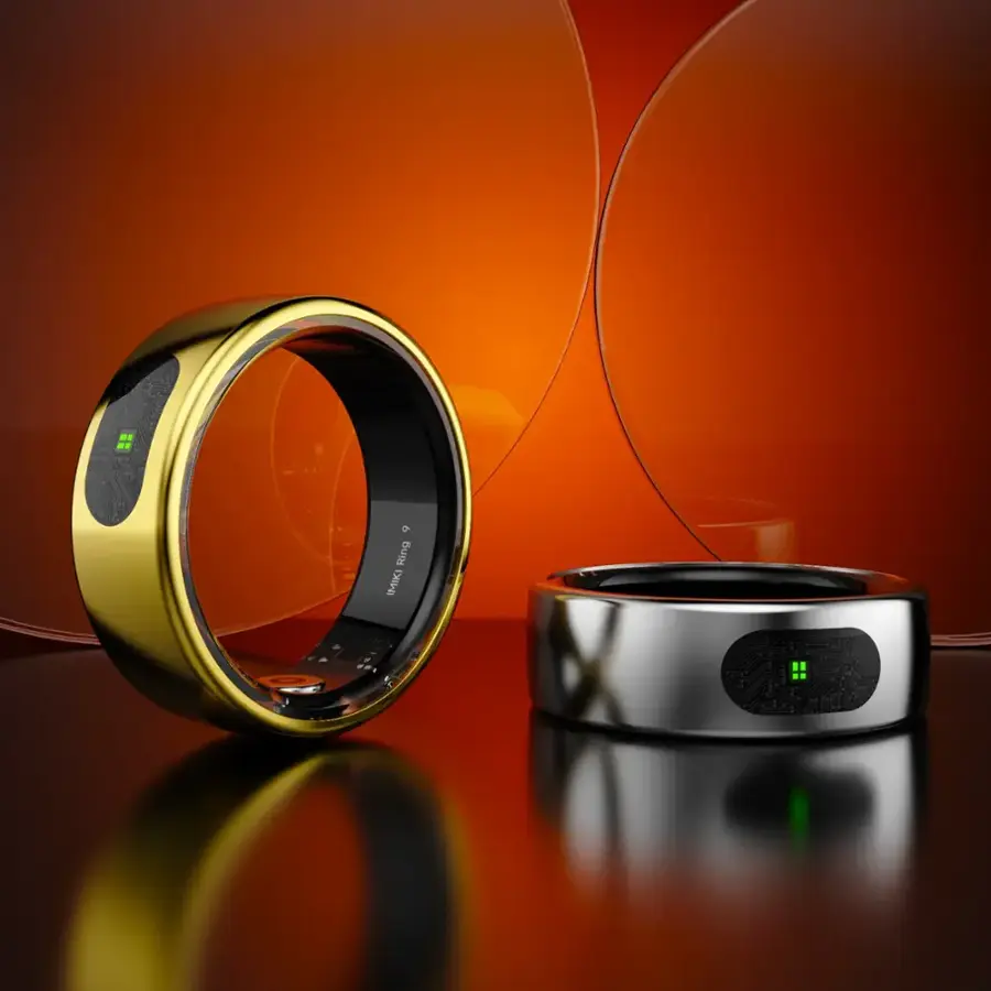 The image features a gold ring and a silver ring, both of which are imikis. The gold ring is placed on a table, while the silver ring is sitting next to it. The rings are displayed in front of an orange background, which adds a vibrant touch to the scene.