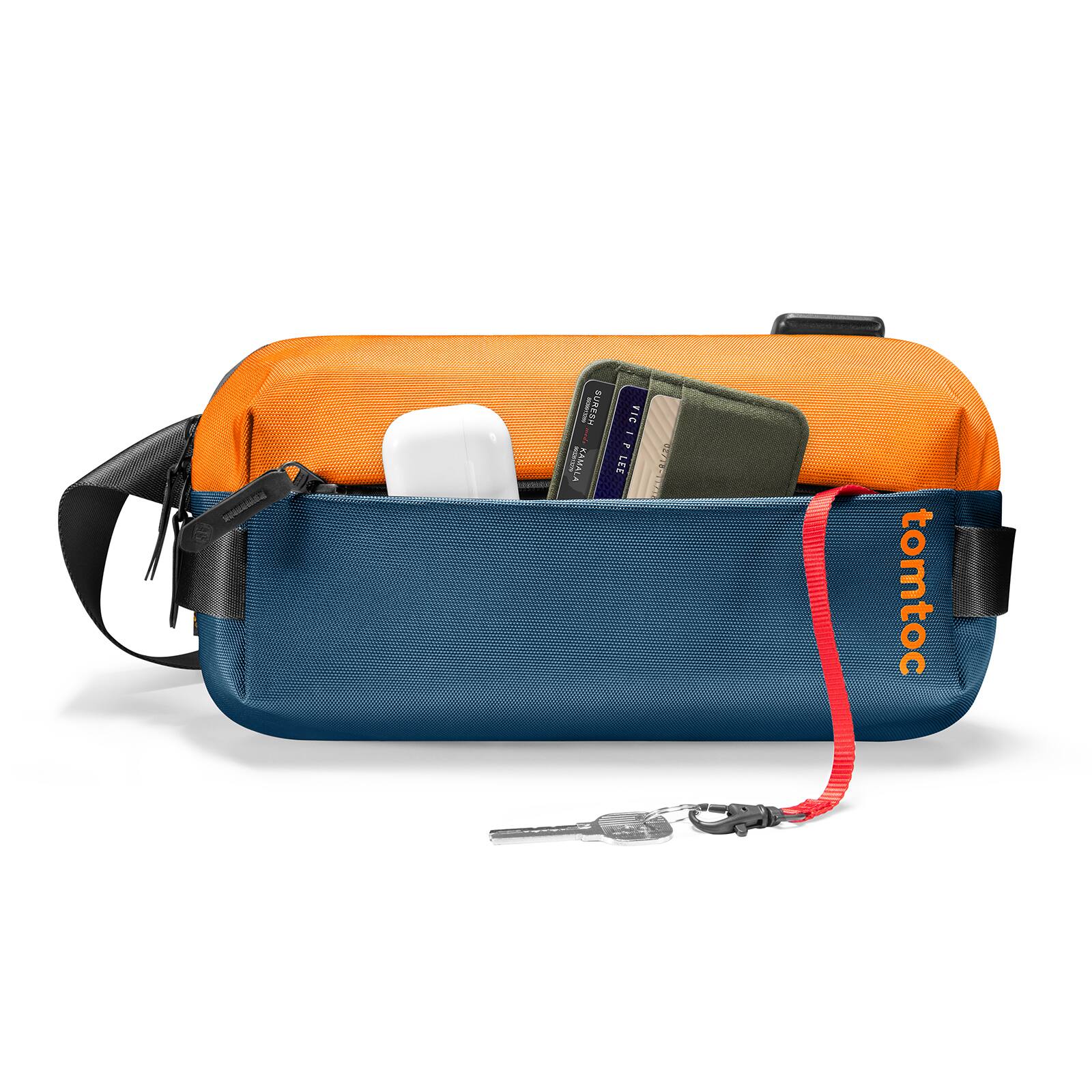 The image features a blue and orange bag with a keychain attached to it. The keychain has a red string and a key attached to it. The bag is filled with various items, including a cell phone, a wallet, and a remote control. The bag is designed by tomtoc, and it appears to be a practical and functional accessory for carrying essential items.