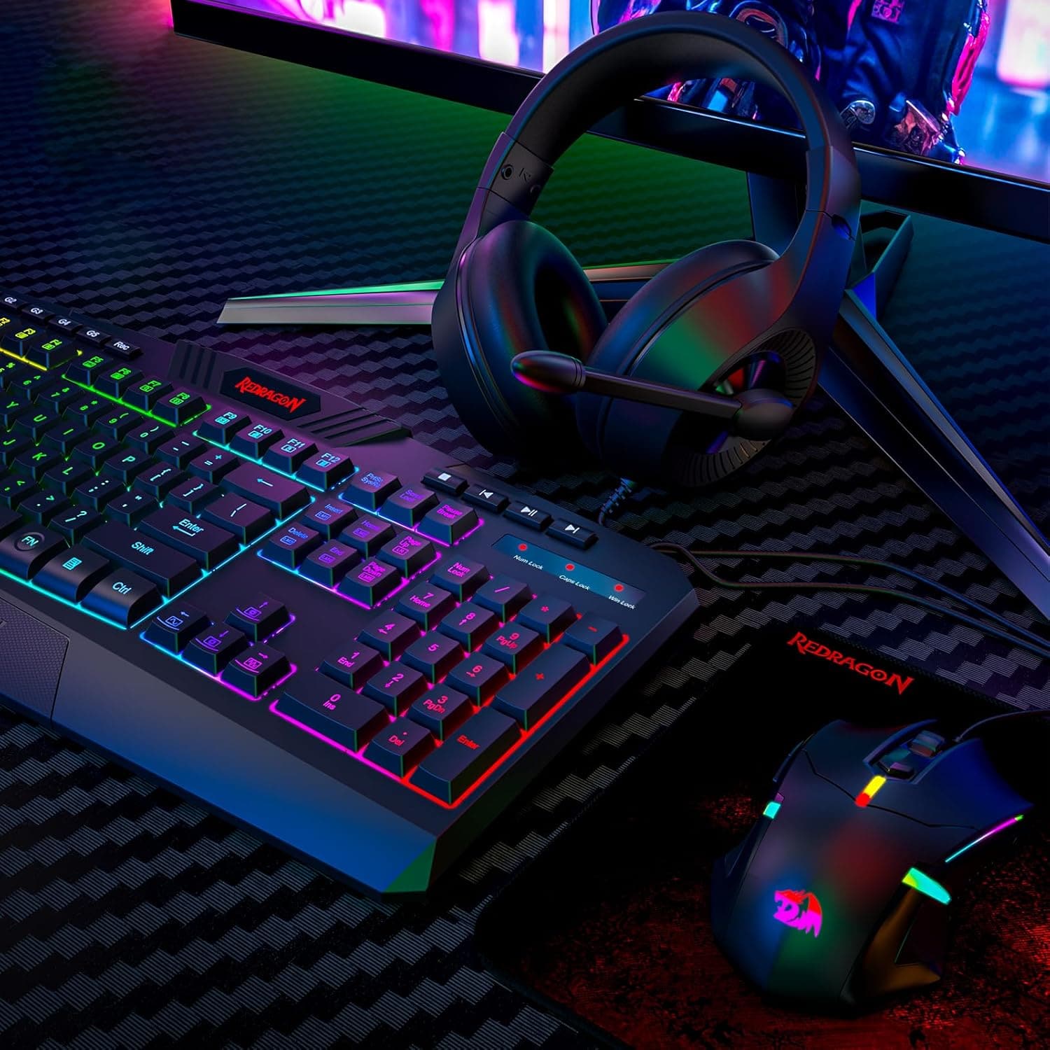 The image features a black and purple keyboard with a colorful design, likely a gaming keyboard, sitting on a desk. Next to the keyboard, there is a mouse and a pair of headphones. The headphones have a colorful design, and the mouse is also colorful. The keyboard is made by Redragon, and the mouse is a 2M. The overall scene suggests a gaming setup or a computer workstation.