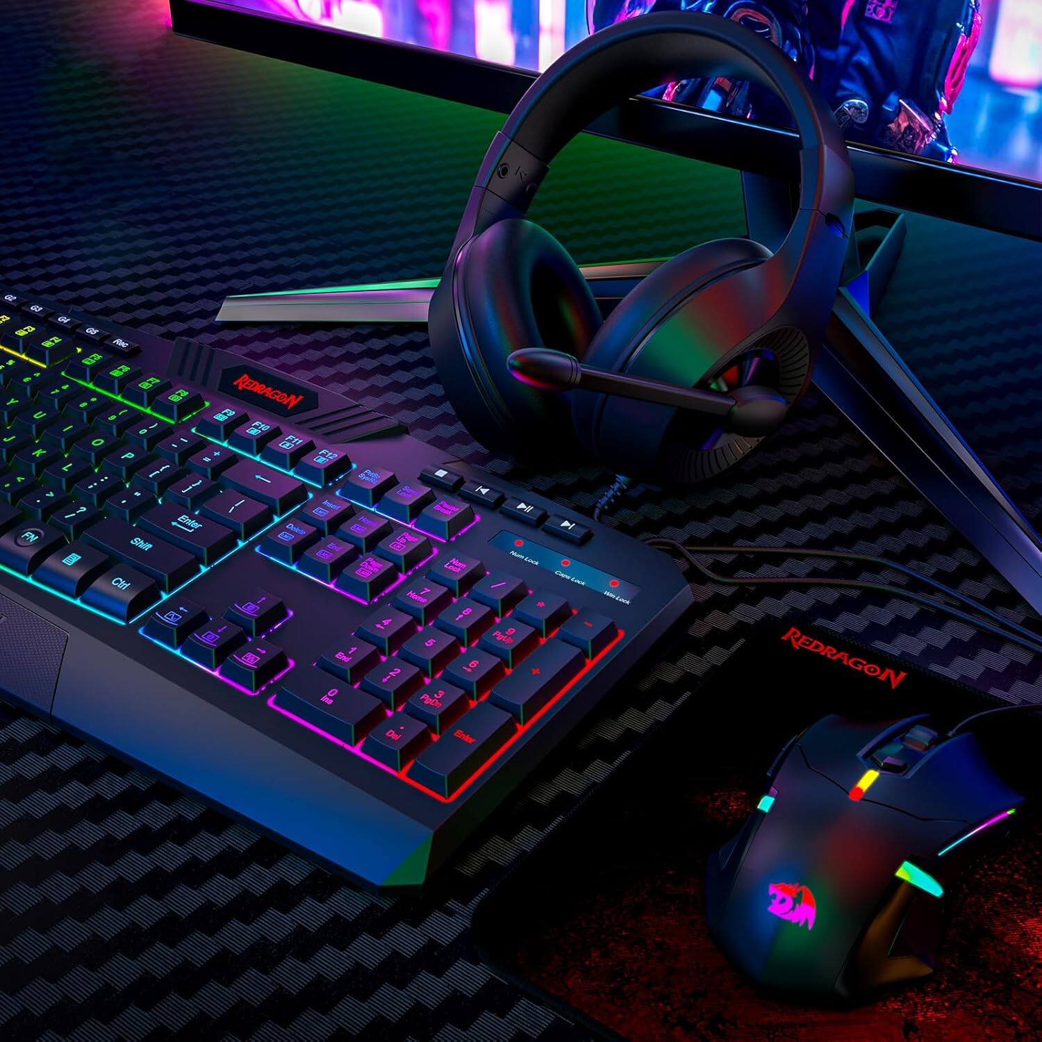 The image features a black and purple keyboard with a colorful design, likely a gaming keyboard, sitting on a desk. Next to the keyboard, there is a mouse and a pair of headphones. The headphones have a colorful design, and the mouse is also colorful. The keyboard is made by Redragon, and the mouse is a 2M. The overall scene suggests a gaming setup or a computer workstation.