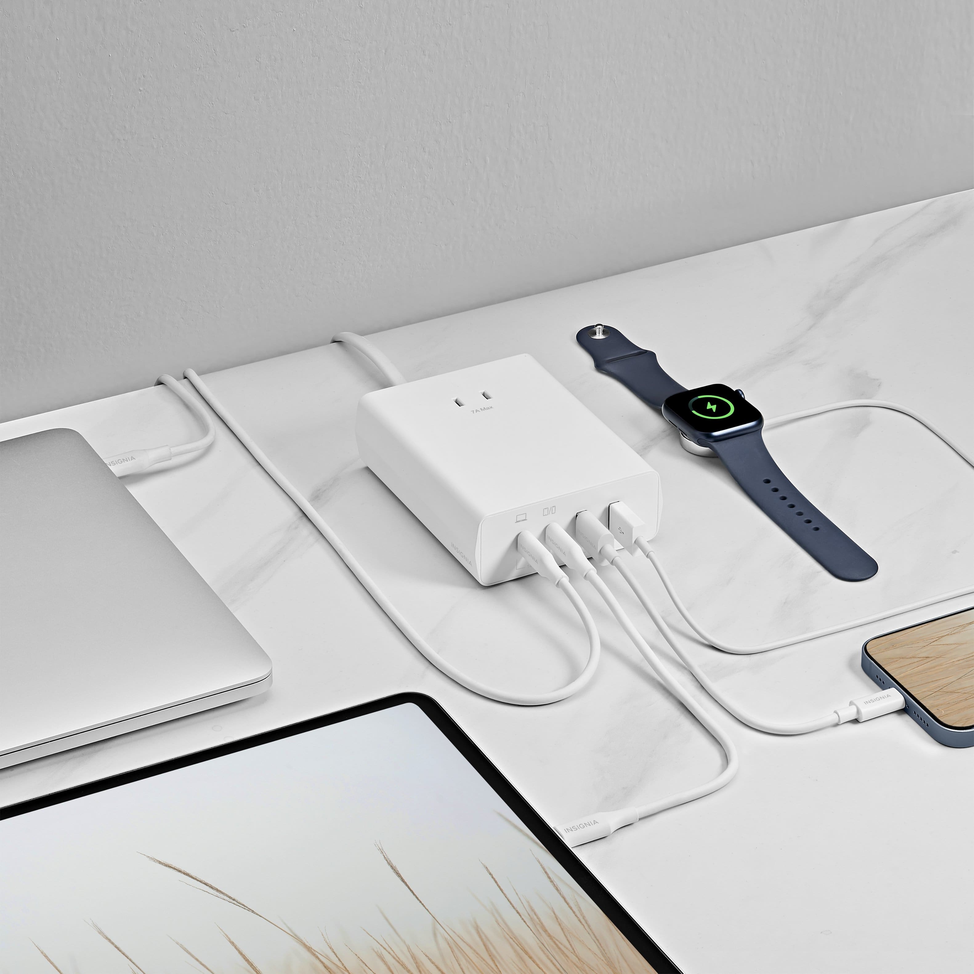 The image shows a desk with a laptop, a cell phone, and a watch. There is also a charger plugged into the wall, and a charger plugged into the laptop. The watch is placed on the table next to the laptop.