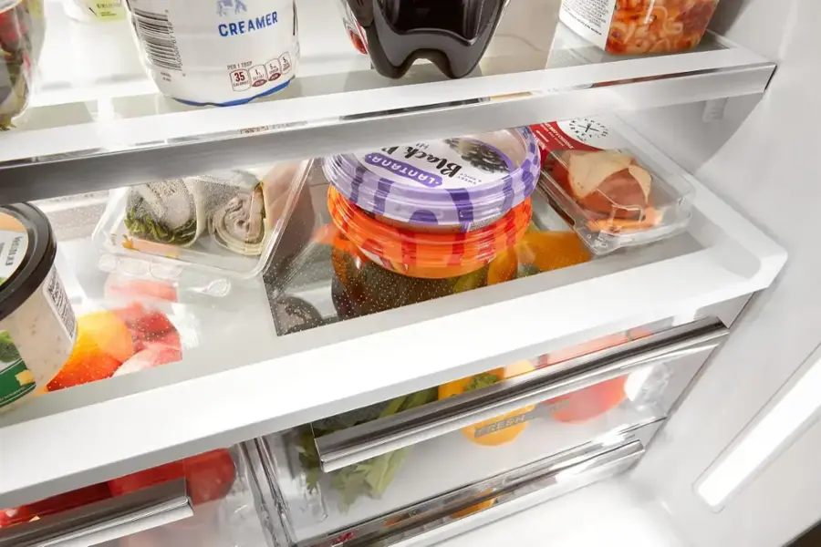 The image shows a refrigerator with various food items inside. The refrigerator contains a container of creamer, a container of black olives, and a container of strawberries. There are also several other containers of food, including a container of oranges, a container of tomatoes, and a container of carrots. The refrigerator is filled with a variety of food items, making it a well-stocked and diverse food storage area.