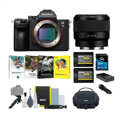 The image features a Sony camera and lens, along with various accessories and items such as a KOAH bag, a KOAH memory card, and a KOAH charger. There are also other items like a book, a bottle, and a remote control. The camera and lens are placed on top of the other items, creating a visually appealing display.