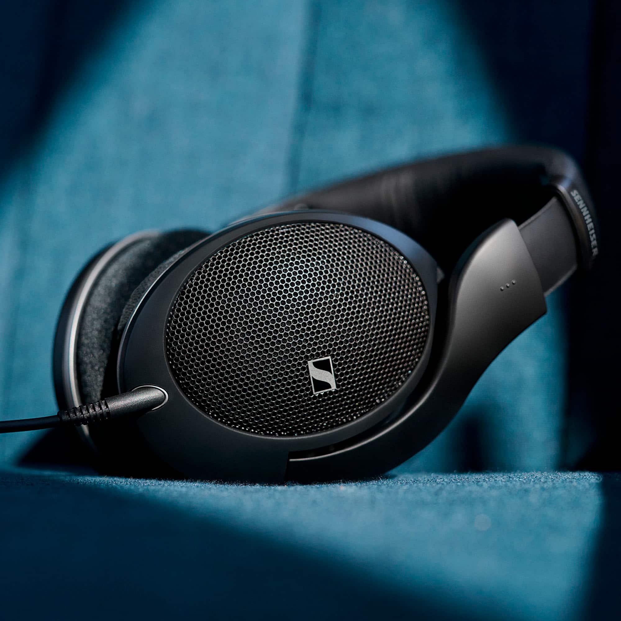 Sennheiser is a brand of headphones known for their high-quality sound and comfortable fit. The image shows a pair of Sennheiser headphones sitting on a blue surface, possibly a couch or a chair. The headphones are black and have a large earpiece, which is typical of Sennheiser's design. The headphones are placed in such a way that they are easily visible and accessible, making them a popular choice for music enthusiasts and professionals who require clear audio for their work.