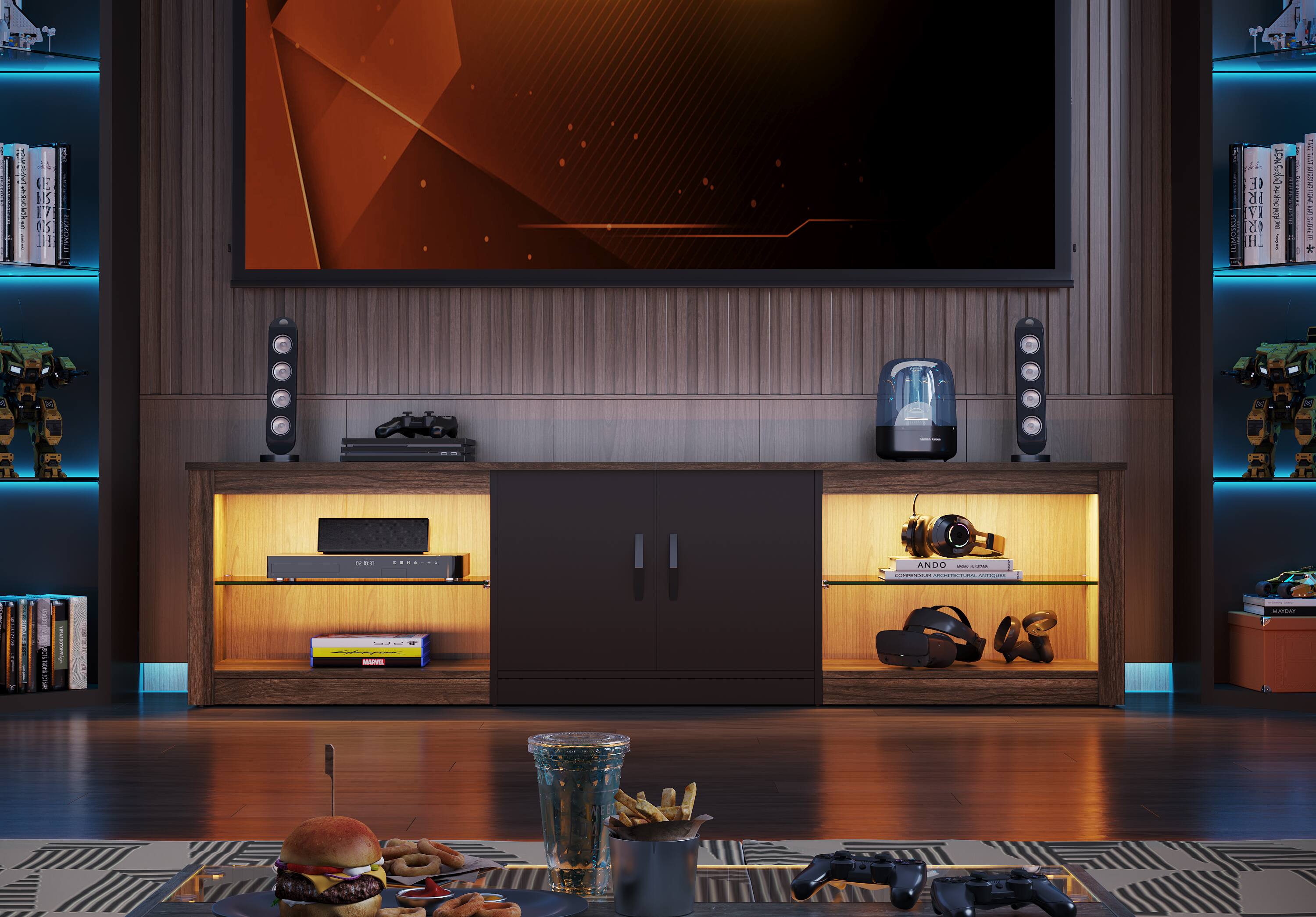 I am a computer-generated image of a living room. The room features a large flat screen TV on the wall, a bookshelf filled with books, and a coffee table with a cup and a sandwich on it. There are also several remotes scattered around the room, indicating that it is a space for entertainment and relaxation.