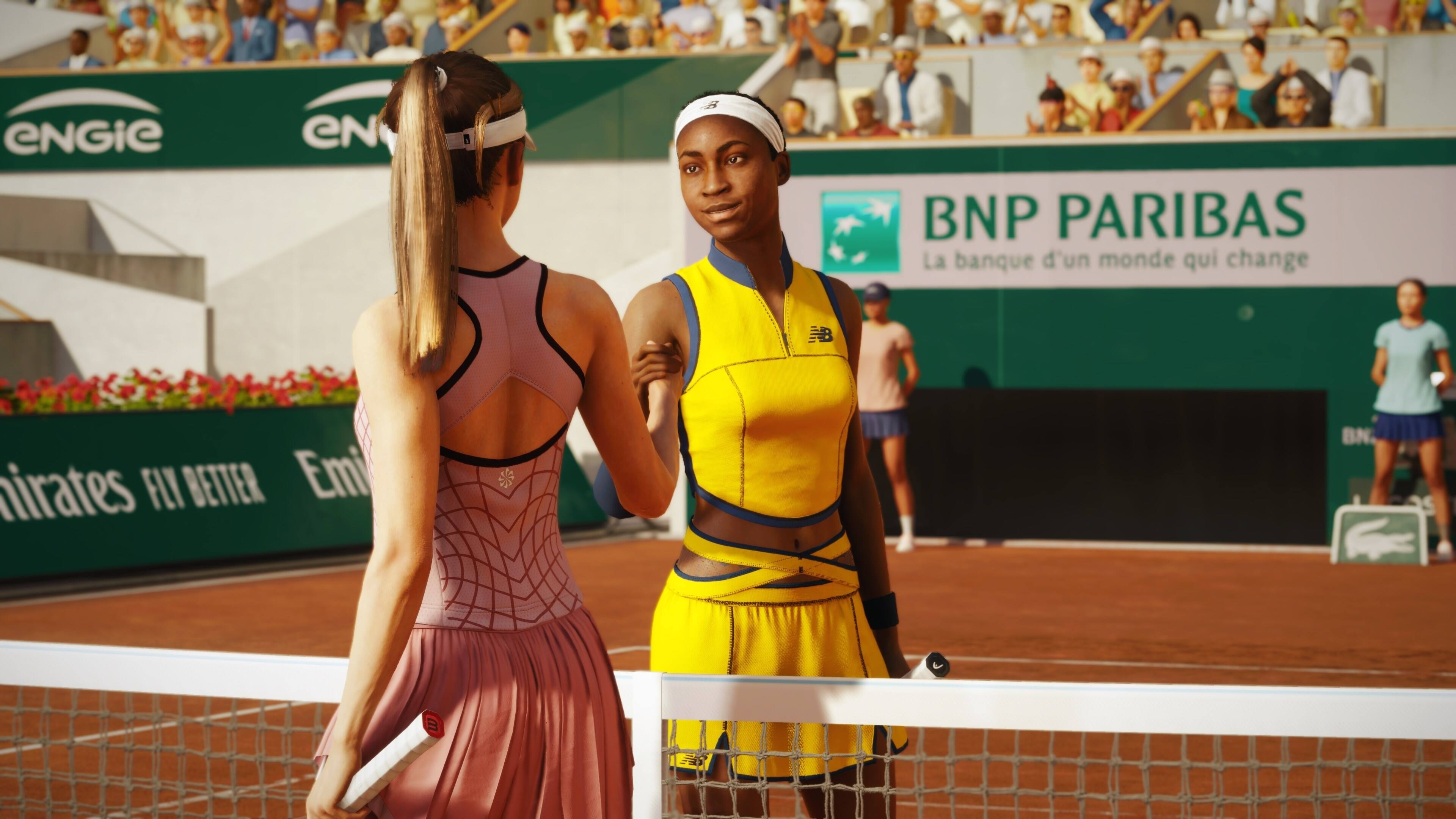 The image features two women playing tennis on a court. One woman is wearing a pink dress, while the other is wearing a yellow outfit. They are both holding tennis rackets and appear to be engaged in a friendly match. The scene is set in front of a crowd of spectators, who are watching the game intently. The image also includes a tennis ball and a chair placed on the court.