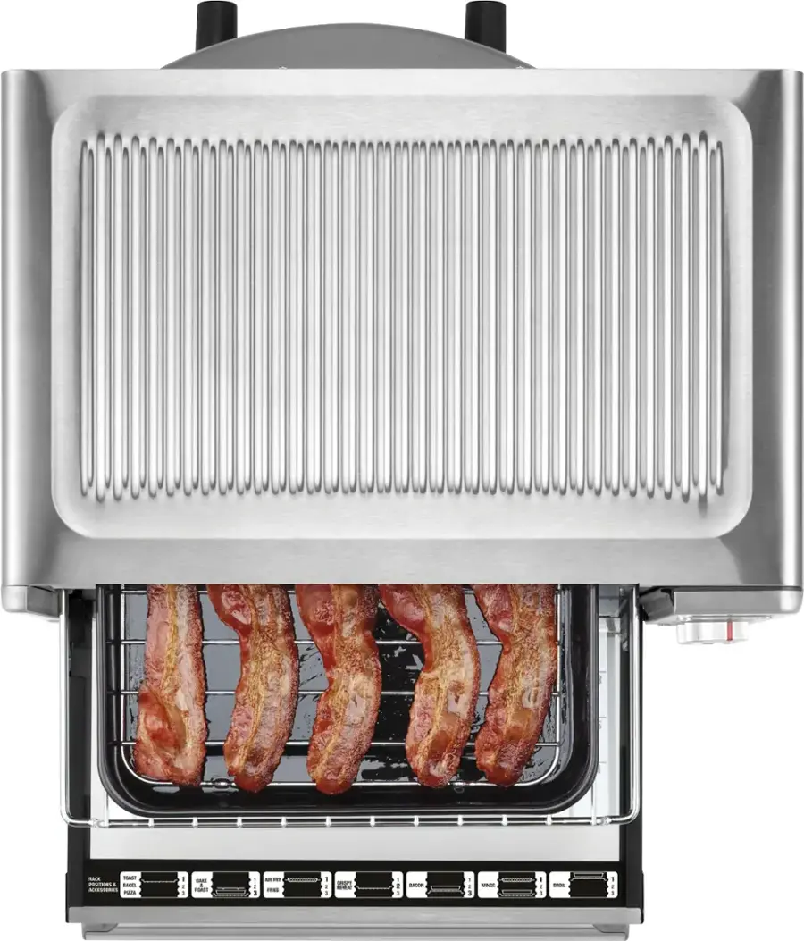The image shows a toaster oven with bacon inside of it. The bacon is placed on a rack and appears to be cooking evenly. The toaster oven is made of stainless steel, giving it a sleek and modern appearance. The bacon is placed in a way that allows it to cook evenly and efficiently, ensuring a delicious and crispy result.