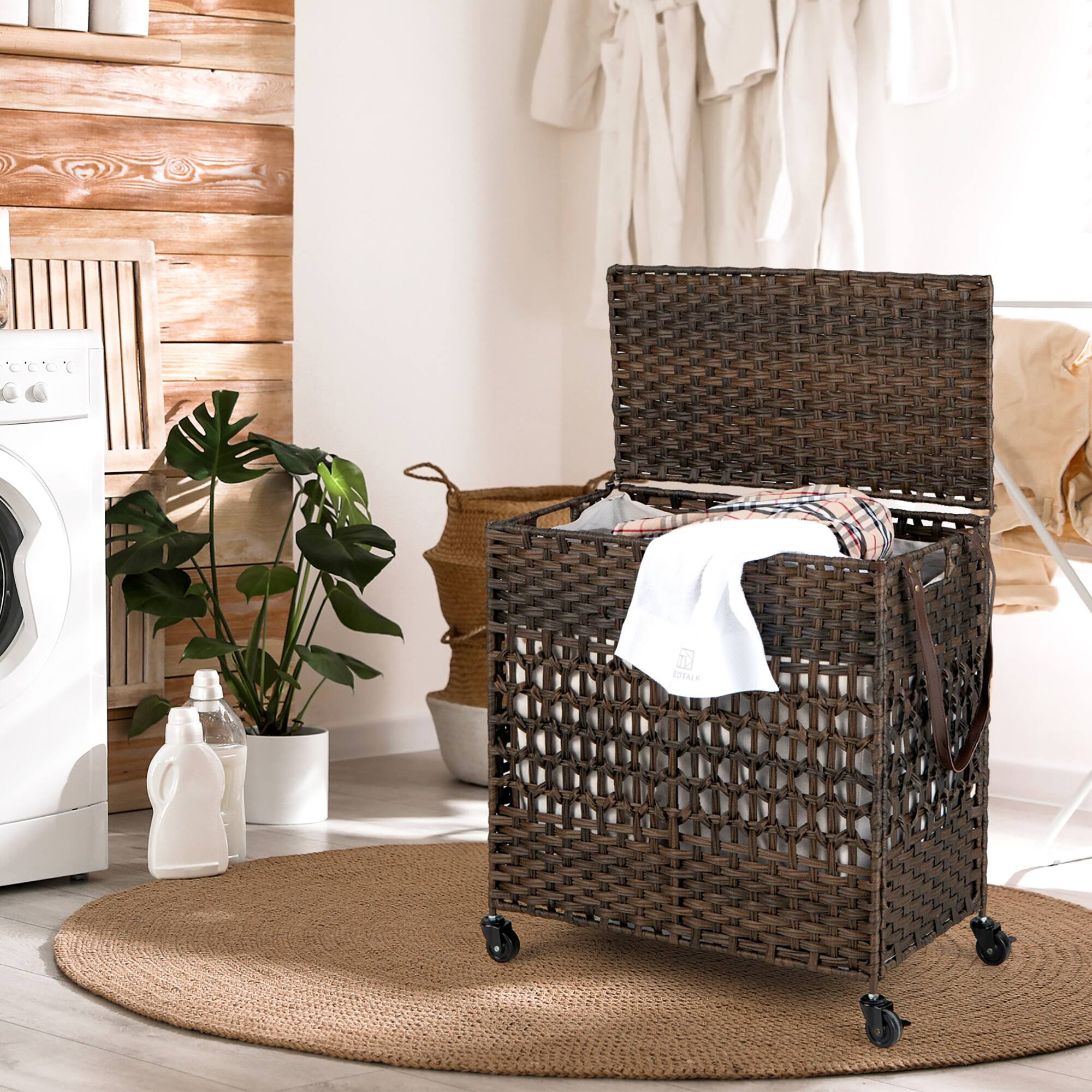 The image shows a wicker basket with clothes in it, placed on a rug. The basket is filled with clothes, and there is a potted plant nearby. The scene also includes a washing machine and a dryer, indicating that the clothes have likely been recently laundered. The overall setting suggests a cozy and organized living space.
