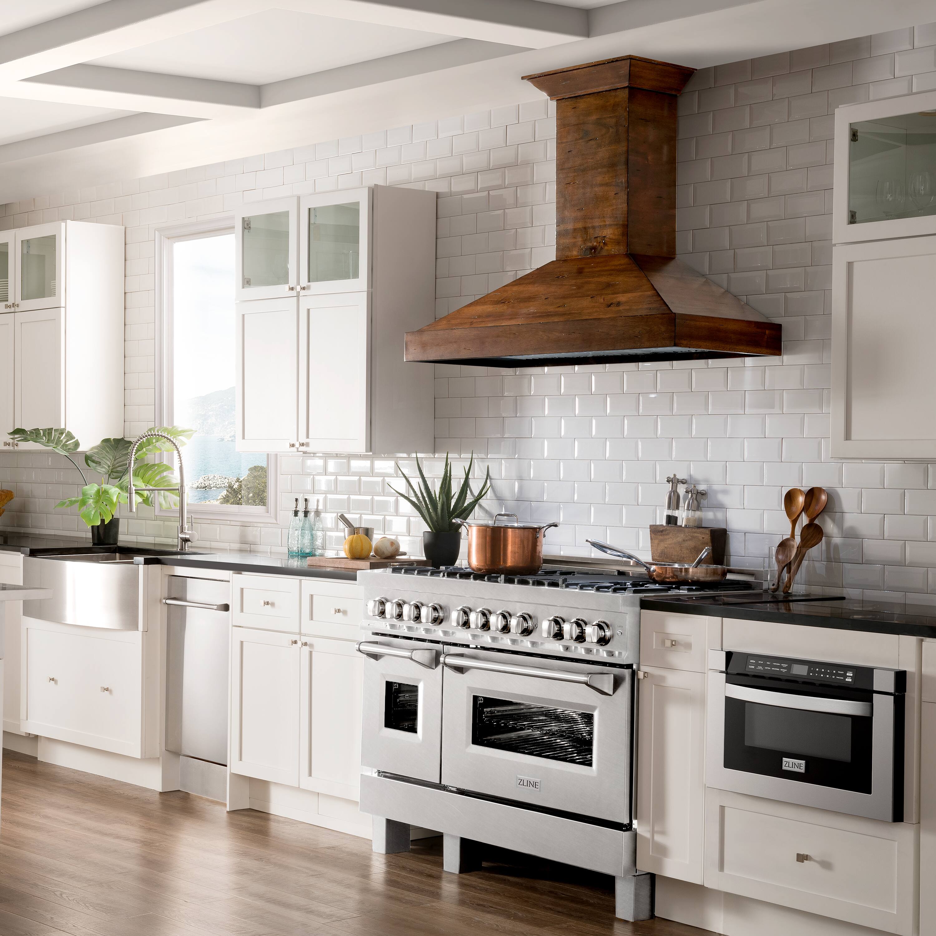 The image shows a kitchen with white cabinets and a stove top oven. The oven is positioned under a ventilation hood, which has a wooden accent. The kitchen also features a sink, a refrigerator, and a window. The countertops are made of marble, and there are several bottles and potted plants placed around the kitchen. The overall design of the kitchen is modern and well-organized.