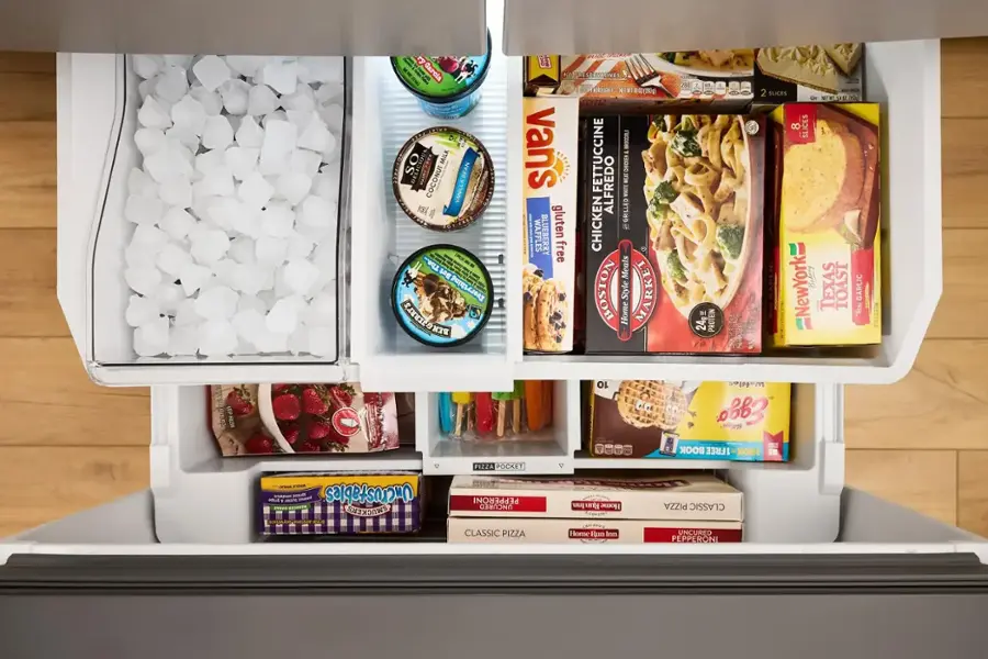 The image shows a refrigerator with its door open, revealing a variety of food items stored inside. There are multiple bottles of milk, including chocolate milk, and several containers of yogurt. Additionally, there are multiple boxes of ice cream, with one of them being vanilla ice cream. The refrigerator also contains a few different types of food, such as pasta, chicken, and waffles. The assortment of food items in the refrigerator suggests that it is well-stocked and ready to provide meals for the household.