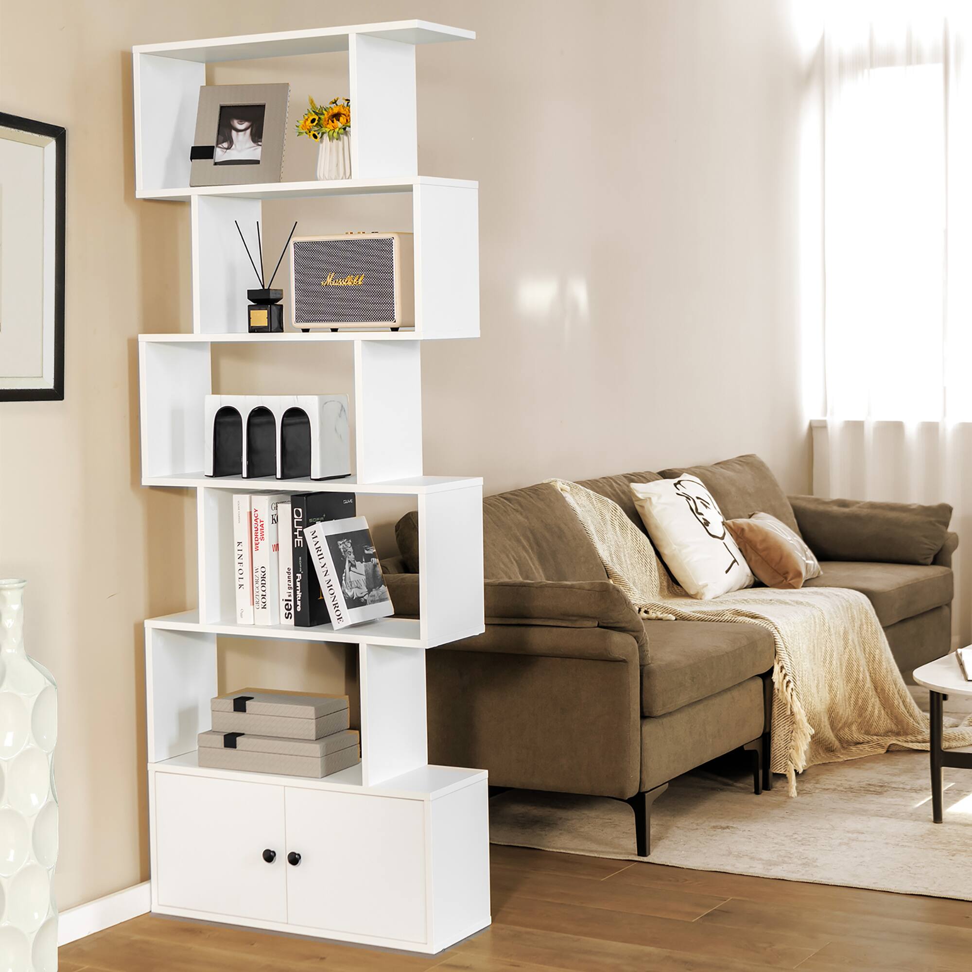 The image shows a living room with a white shelf and a bookcase. The shelf is filled with various items, including a radio, a vase, and a few books. The bookcase is also filled with books, creating a cozy and organized atmosphere in the room. The living room is furnished with a couch and a chair, providing a comfortable space for relaxation and reading.