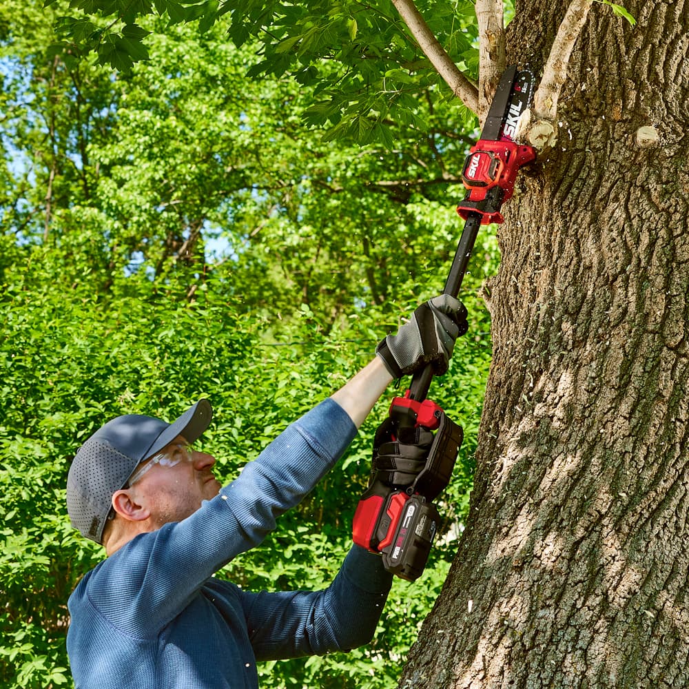 The man is using a Skil saw to cut into a tree.