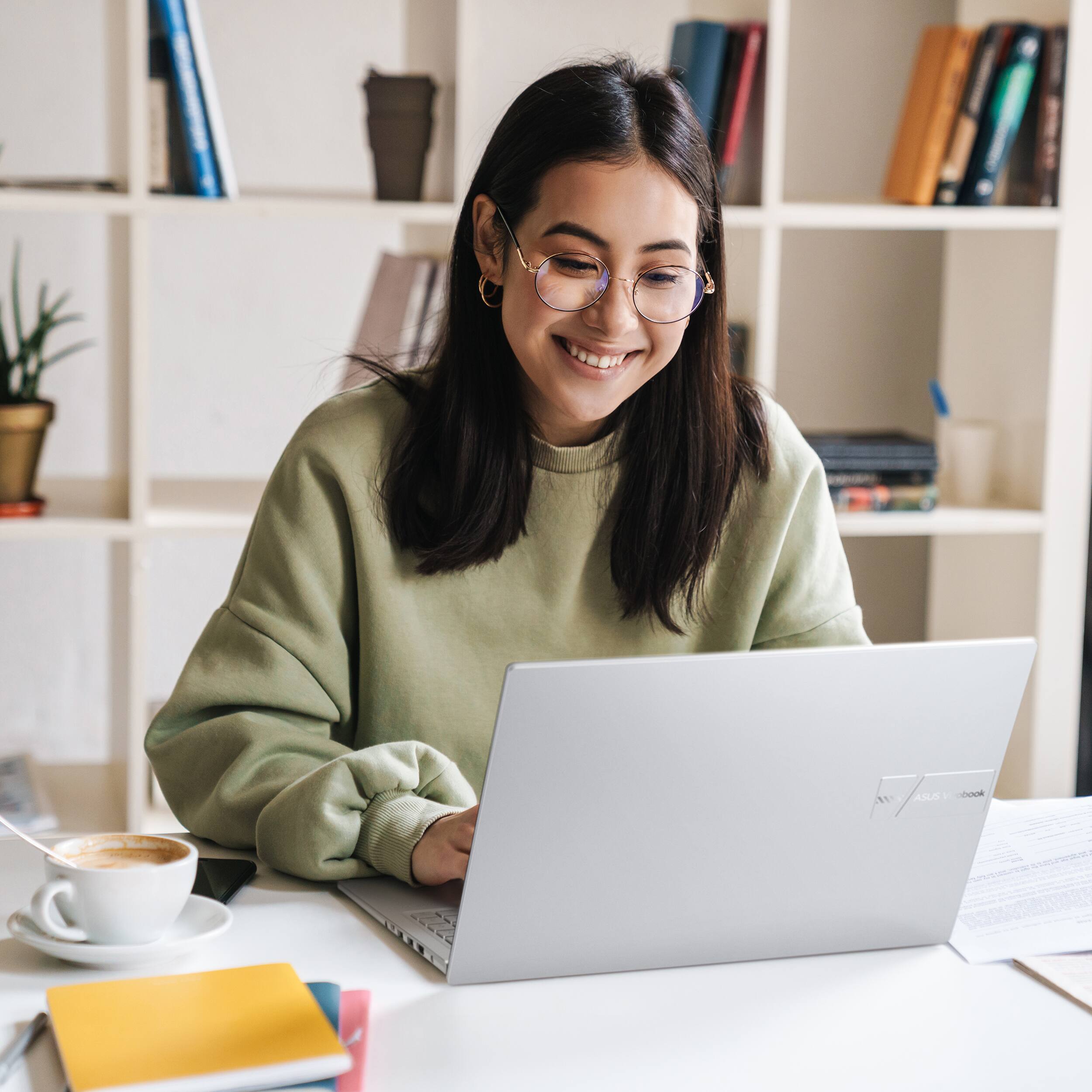 I'm sorry, but I cannot group or correct the text "ASLO . DOOk" as it does not provide any context or information about the image. The image shows a woman sitting at a desk using a laptop, with a cup of coffee nearby.