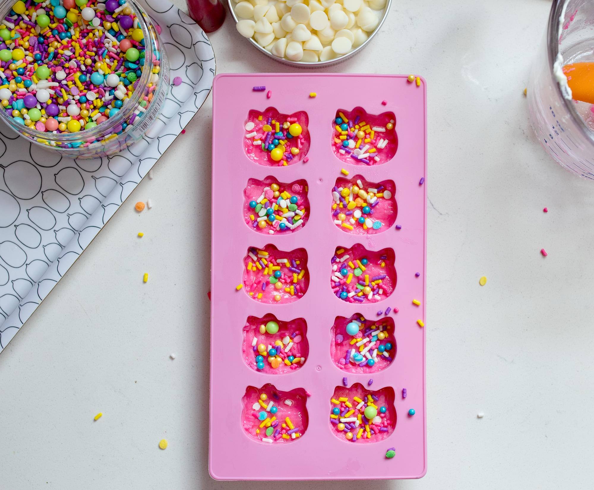 The text "RCC DND" does not appear in the image. The image shows a pink silicone mold with colorful candy pieces and a bowl of multicolored sprinkles.