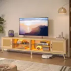 The image features a large flat screen TV sitting on top of a wooden entertainment center. The TV is turned on, displaying a beautiful sunset on the screen. The entertainment center has two shelves, one of which is filled with various items such as books, remotes, and a vase. The other shelf is empty, providing a clean and organized look to the entertainment area. The room also has a potted plant and a lamp, adding to the cozy and inviting atmosphere.