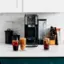 The image features a counter with a Ninja coffee maker and two glasses of iced coffee. The coffee maker is placed between the two glasses, which are filled with the refreshing beverage. The counter also has a few books and a knife set nearby, adding to the cozy and functional atmosphere of the space.