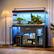 I have a 10 gallon tank with a variety of fish and plants. The tank is filled with water and has a blue light on top. The tank is located in a room with a wooden floor and a lamp nearby. There are also some bottles and a potted plant in the room.