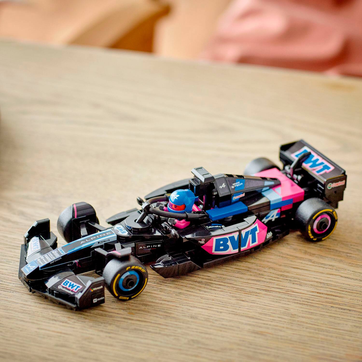 BWT Alpine F1 Team is the name of the racing team that sponsors this race car. The car is painted in blue, pink, and black colors, and it is sitting on a wooden table. The car is a toy or a model, and it is likely displayed as a collectible or a decoration.