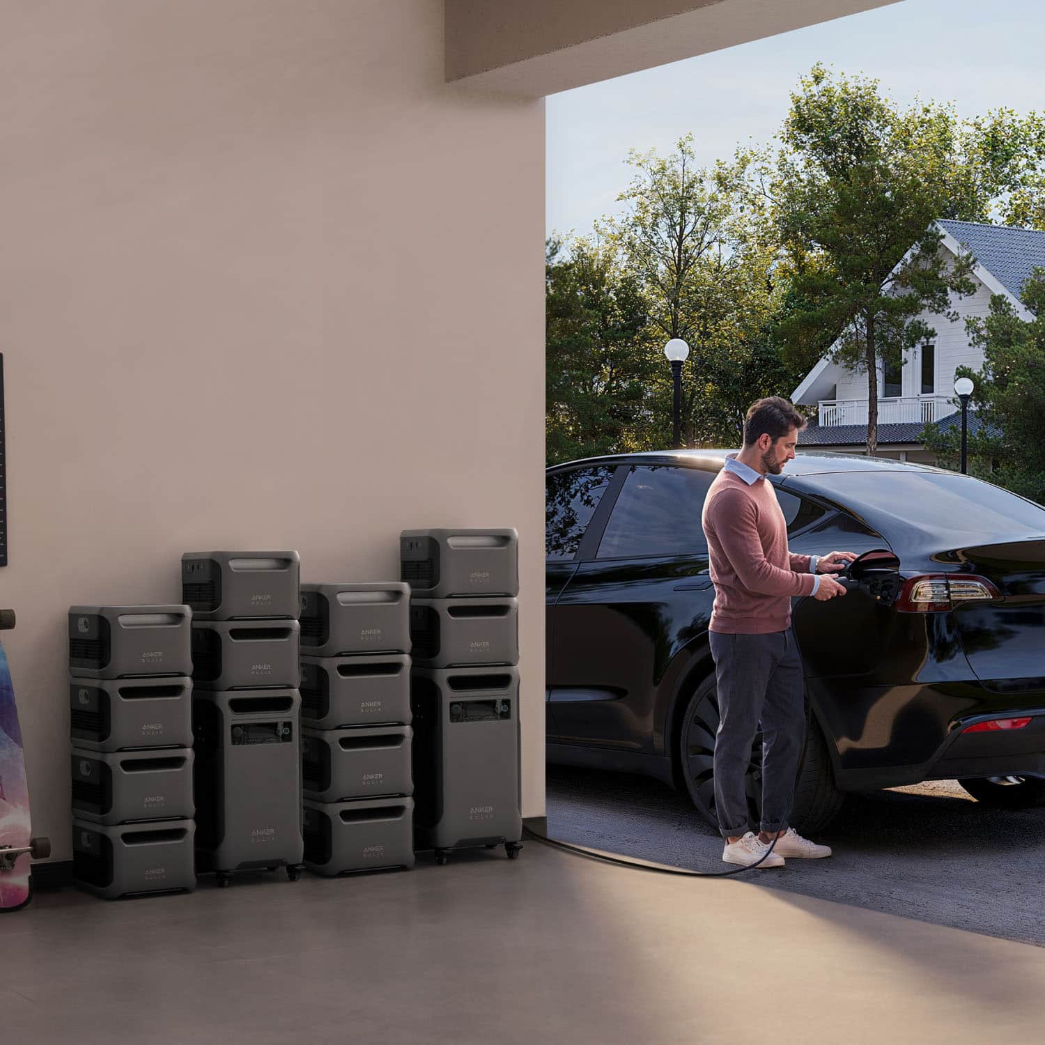 The man is standing outside of his car, which is parked in a driveway. He is plugging his car into a charger, likely to charge the electric vehicle. The scene takes place in front of a house, and there are several stacks of items nearby.