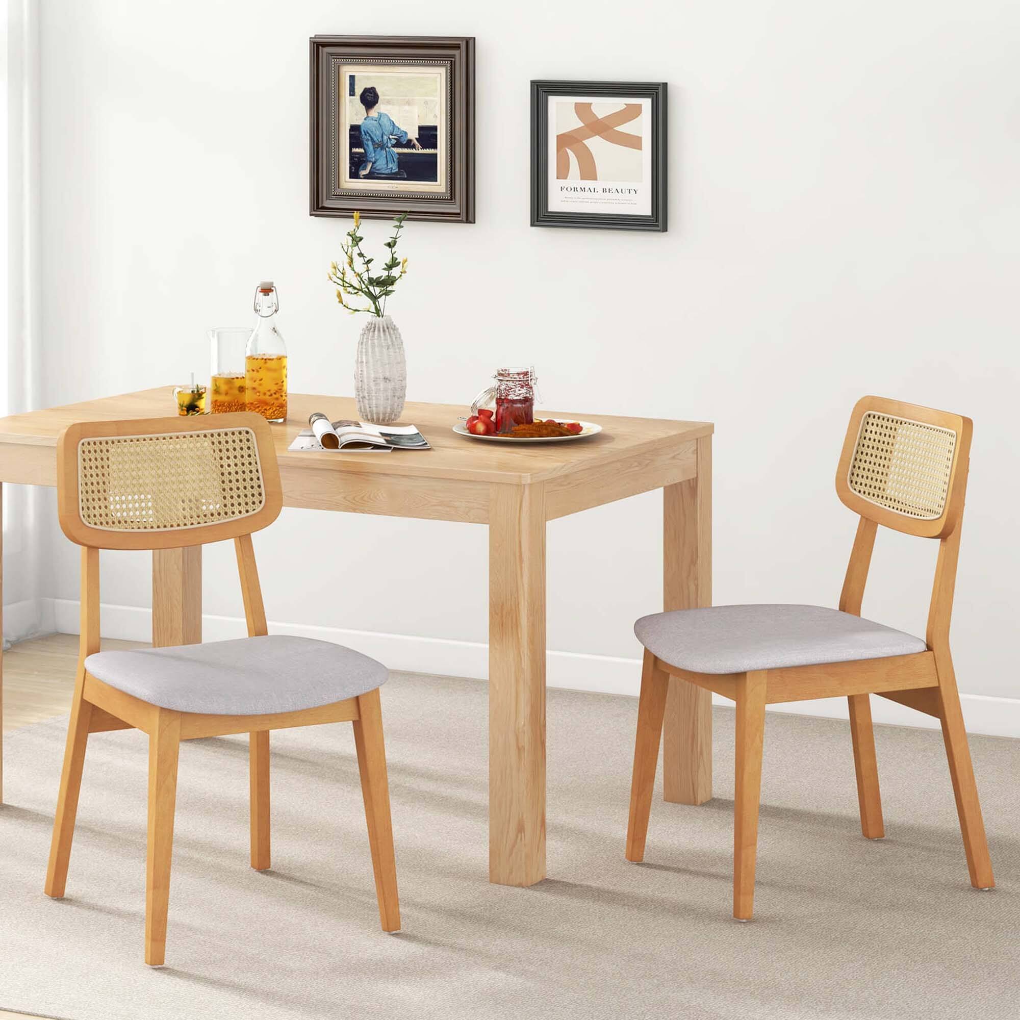 The image shows a wooden dining table with four chairs surrounding it. The table is set with a vase of flowers, a bottle, a cup, a spoon, and a bowl of fruit. The chairs are arranged around the table, creating a cozy and inviting atmosphere for a meal or gathering. The table is positioned in a corner, making it a functional and attractive addition to the room.